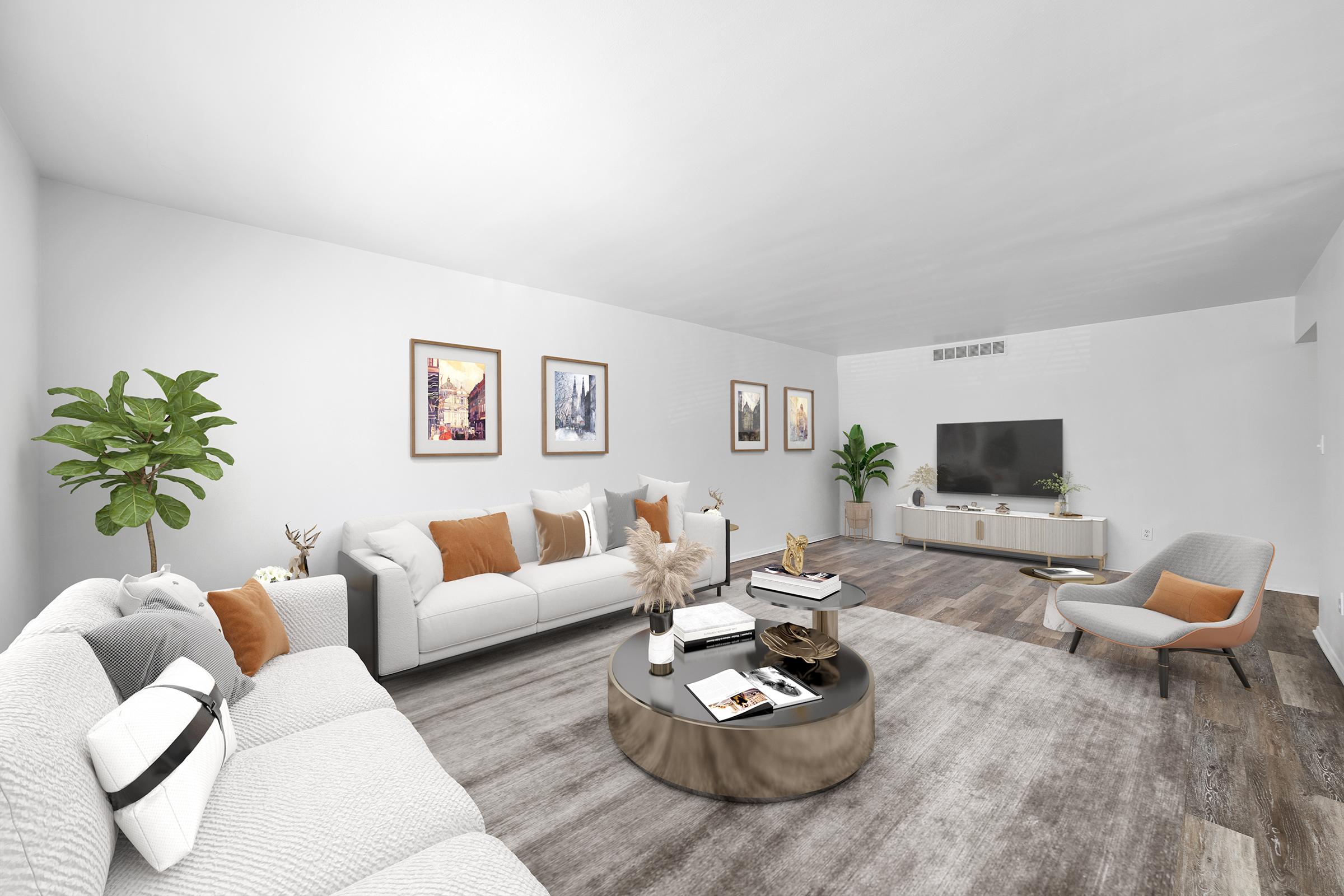 A modern living room featuring a white sofa with orange and cream pillows, a round coffee table with decorative items, and a cozy armchair. The walls are adorned with framed artworks, and there are green plants enhancing the aesthetic. A TV is mounted on the wall, and the flooring has a stylish wooden finish.