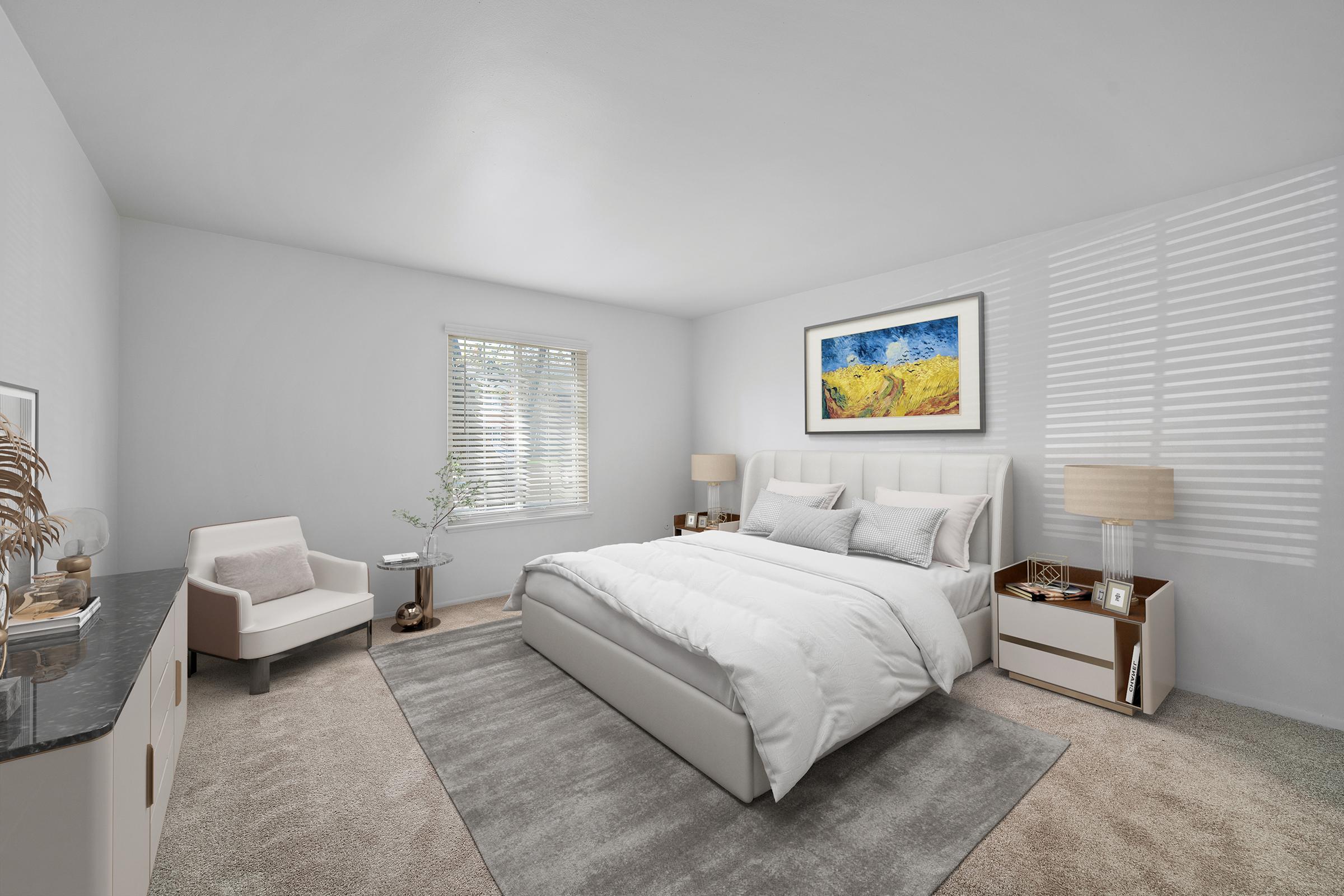 Modern bedroom featuring a queen-sized bed with white bedding, two bedside tables with lamps, and a light gray area rug. A cozy armchair sits in one corner, and a large window allows natural light to fill the room, complemented by a colorful abstract painting on the wall. Neutral-toned walls and carpet create a serene atmosphere.