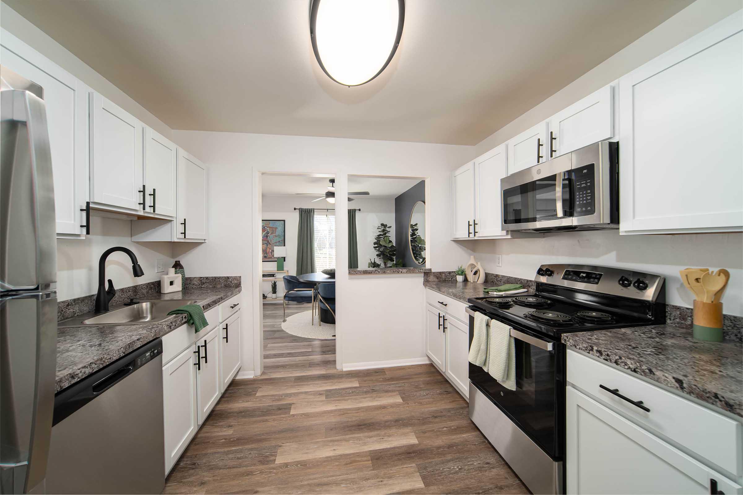 Modern kitchen featuring white cabinetry, granite countertops, stainless steel appliances, and a center island. The space is well-lit with a ceiling light, and there are decorative elements like kitchen utensils and plants, creating a warm and inviting atmosphere.