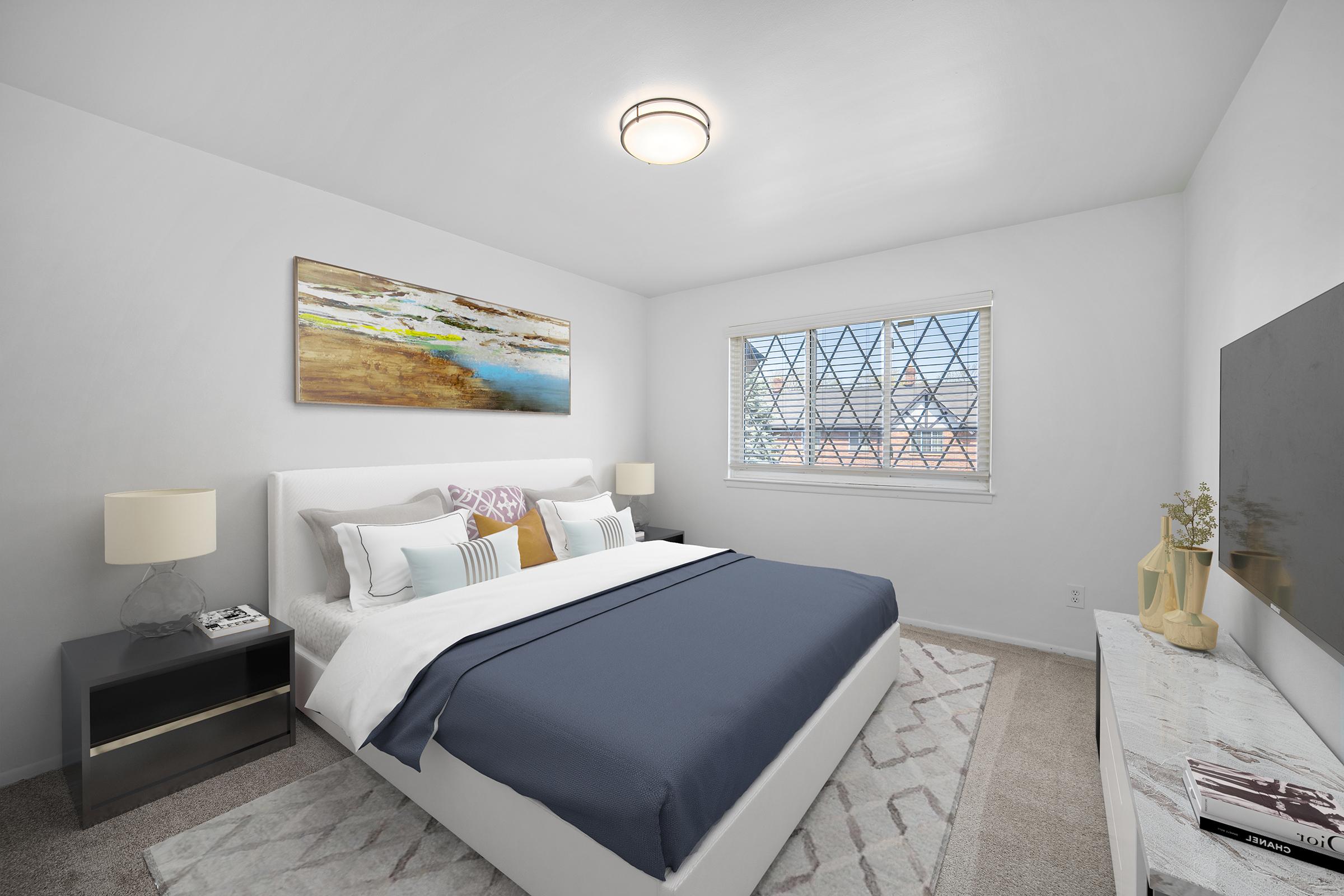 A bright and modern bedroom featuring a queen-sized bed with white and navy bedding, a colorful abstract painting above the bed, and two bedside lamps. A window with grid patterns allows natural light in, and there's a stylish dresser against one wall, creating a cozy and inviting atmosphere.