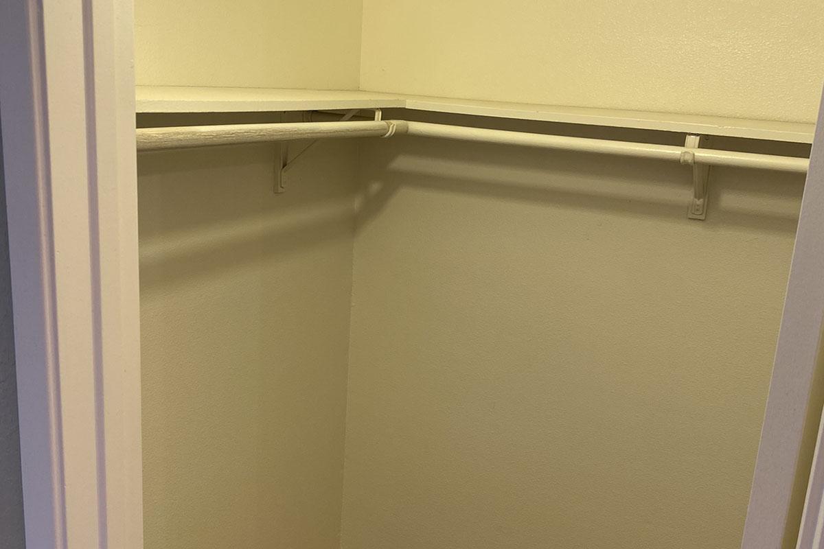 An empty closet with light yellow walls and a single hanging rod. The closet is sparsely furnished, with no shelves or items visible inside, creating a clean and minimalist appearance. The area is well-lit and appears to be well-maintained.