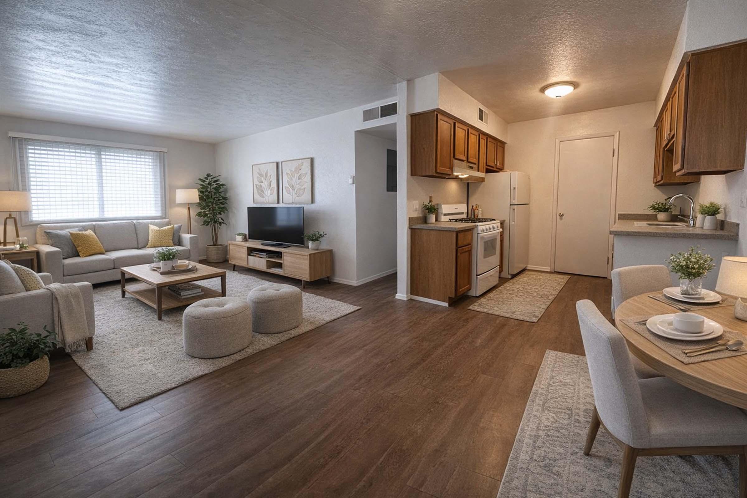 A modern living space featuring a cozy living room with a sofa, coffee table, and TV, complemented by warm lighting. The open kitchen includes wooden cabinets and white appliances. A dining area with a round table and chairs is visible, creating a welcoming atmosphere. Soft rugs and plants enhance the decor.