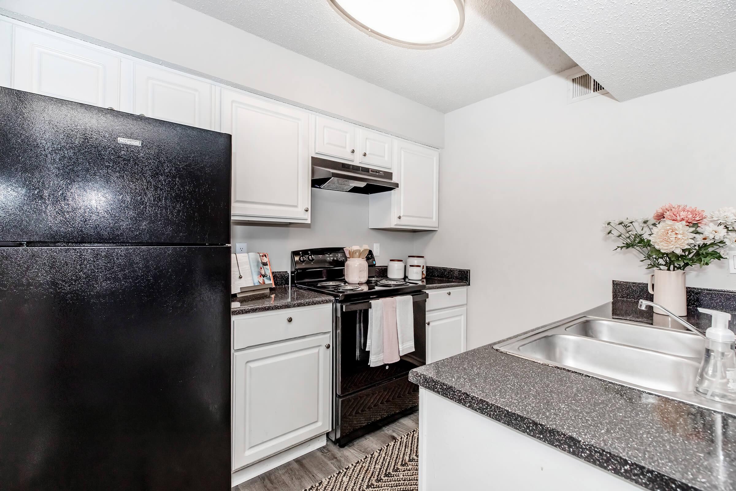 Modern kitchen featuring white cabinets, a black refrigerator, and a black stove. The countertop is dark with a sink on one side, and there are decorative items including a floral arrangement. The space is well-lit and organized, highlighting a clean and inviting atmosphere.