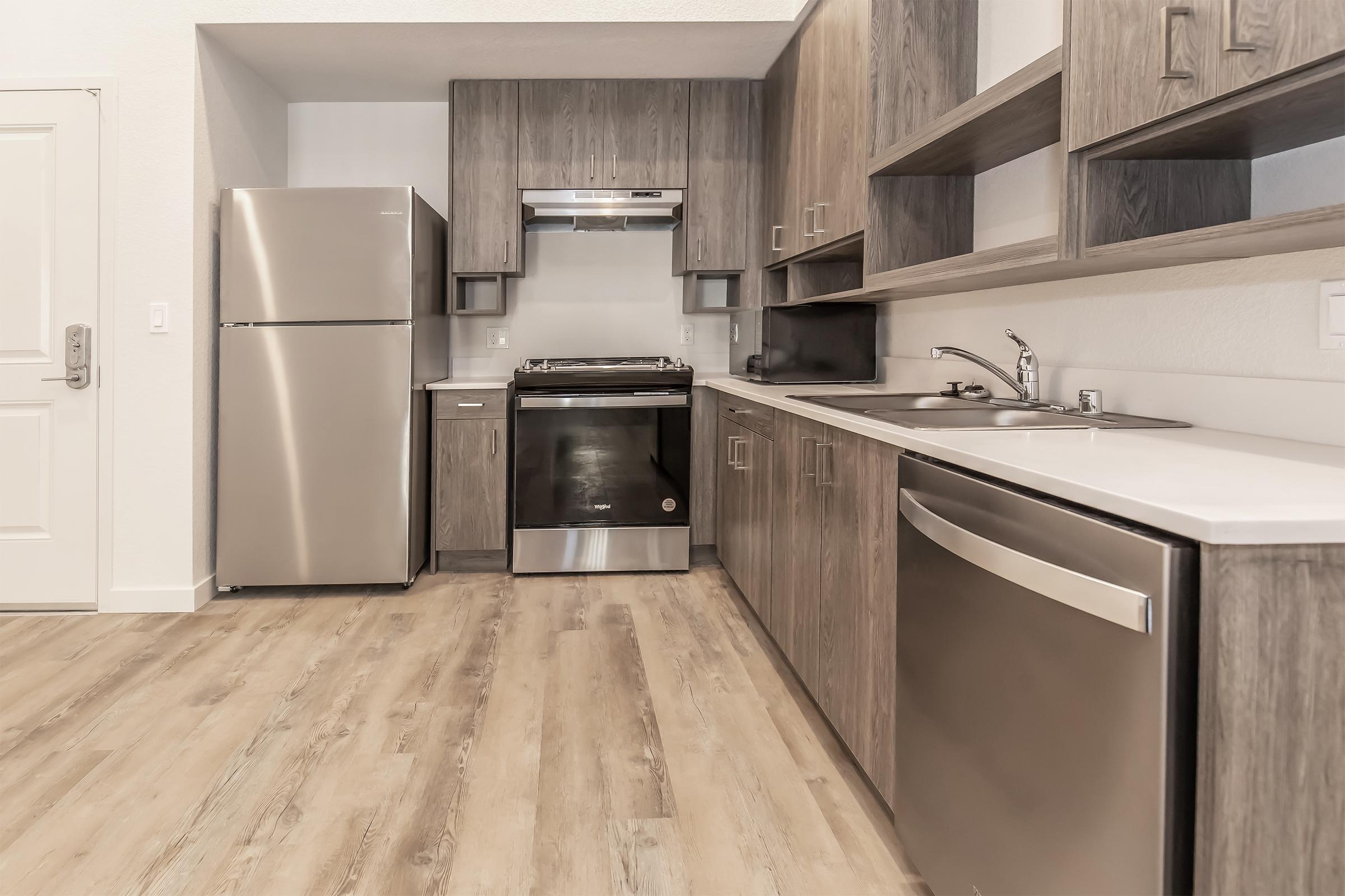 Modern kitchen featuring stainless steel appliances, including a refrigerator, oven, and dishwasher. The cabinets are a warm wood finish, with sleek countertops providing a clean and contemporary look. Light hardwood flooring completes the inviting space.