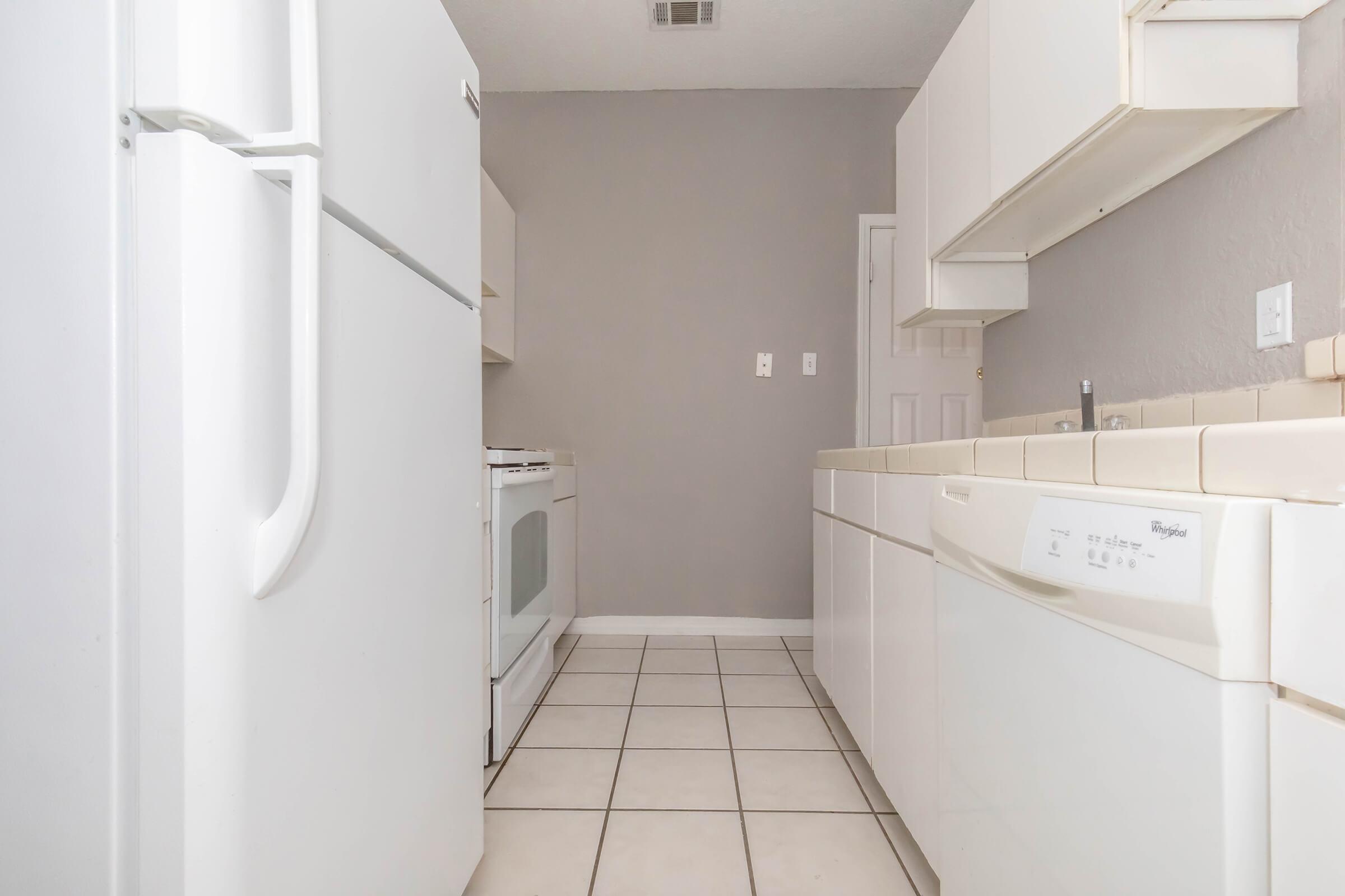 A clean, modern kitchen featuring white appliances, including a refrigerator and stove, with light-colored cabinets and a tiled floor. The walls are painted a soft gray, creating a bright and inviting atmosphere.