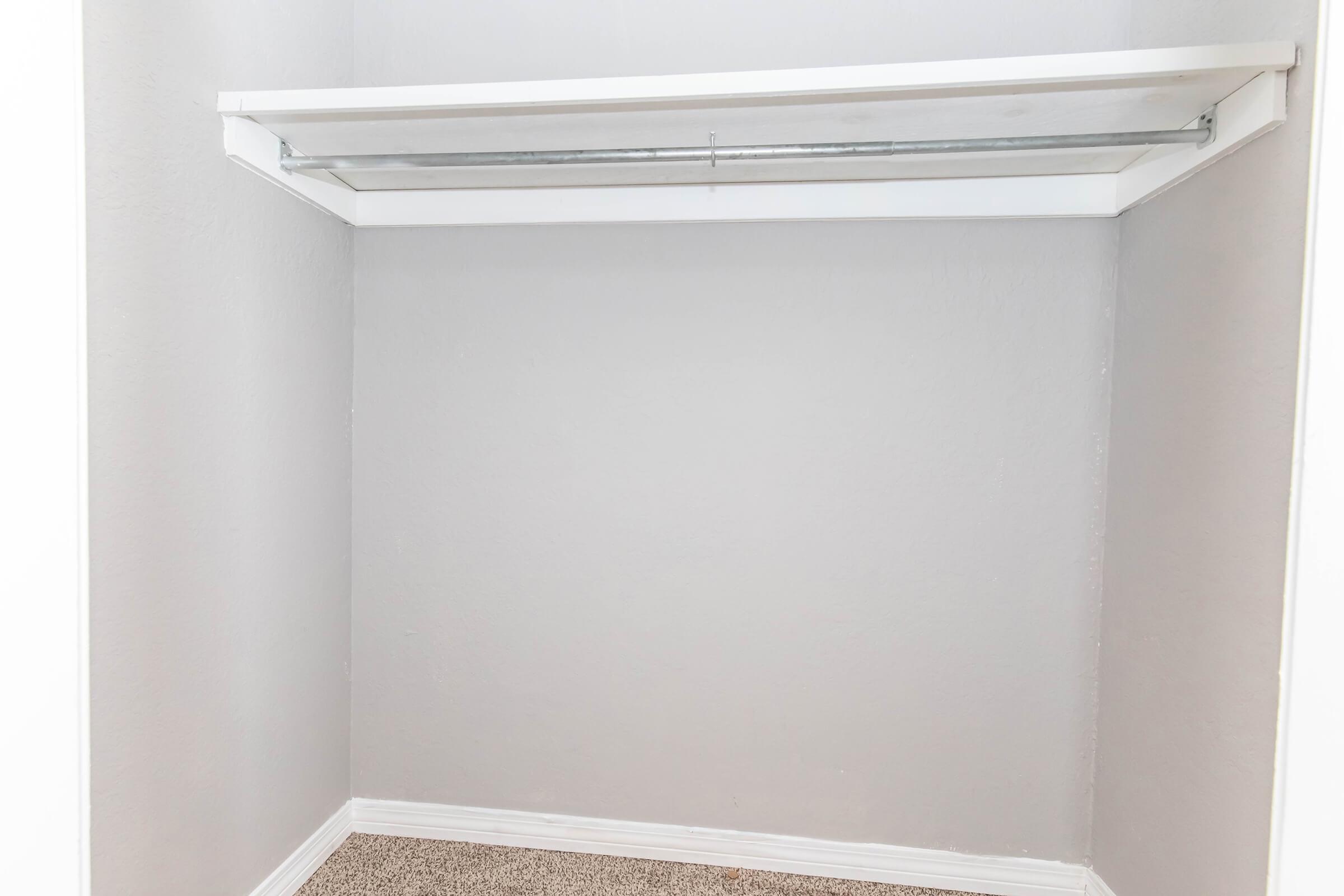 Empty closet with a white shelf above a light gray wall. The floor is carpeted in a light color.