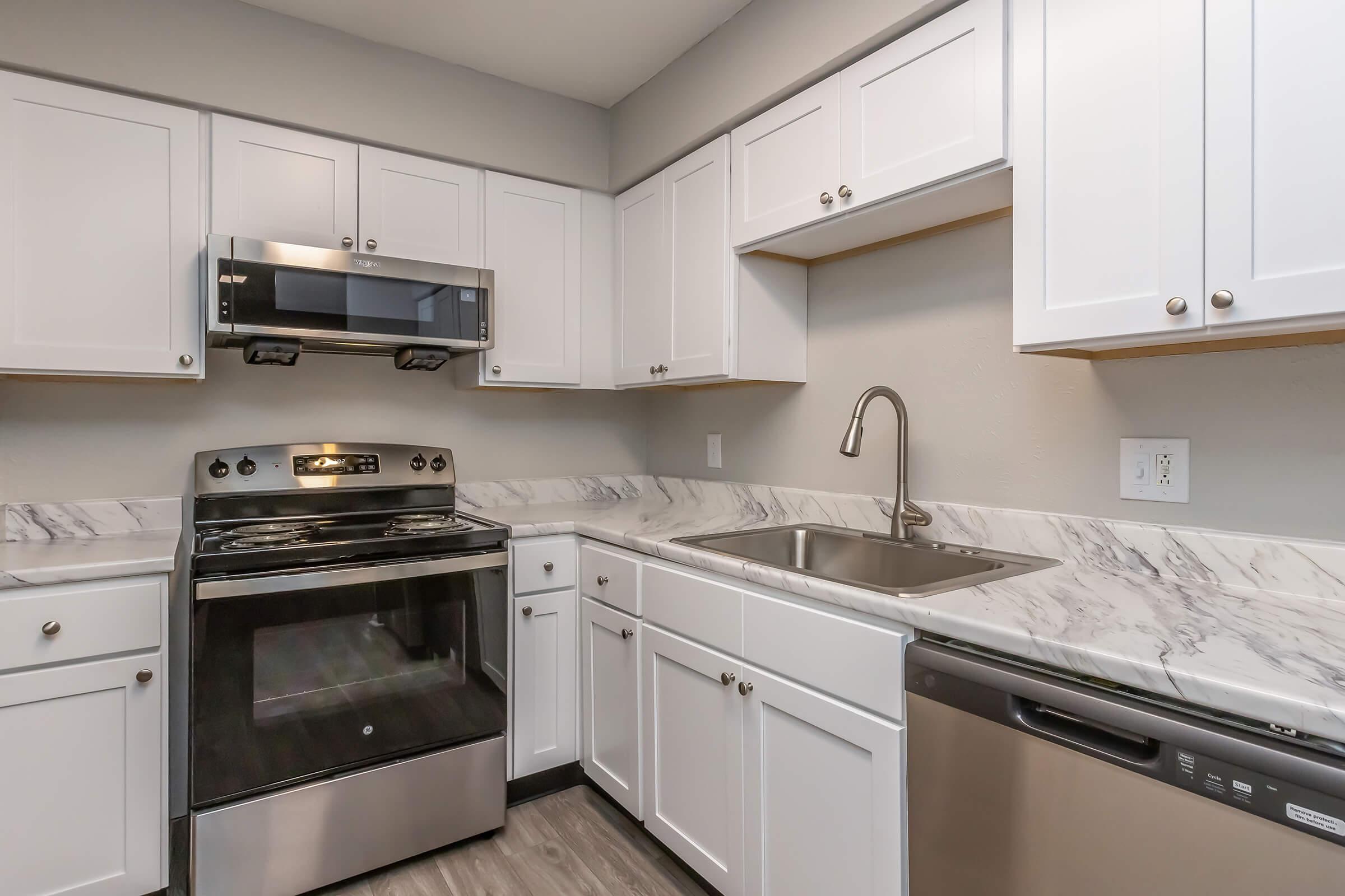 A modern kitchen featuring white cabinets, stainless steel appliances, a gas stove with an oven, a sleek sink with a faucet, and a marble countertop. The design is clean and contemporary, with a focus on functionality and simplicity.