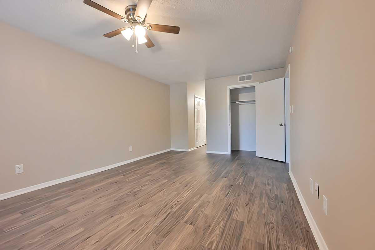 Spacious room with light wood flooring and a ceiling fan. The walls are a neutral beige, and there is a doorway leading to a closet area. A second door is visible on the right, suggesting access to another part of the space. Natural light brightens the room, creating an inviting atmosphere.