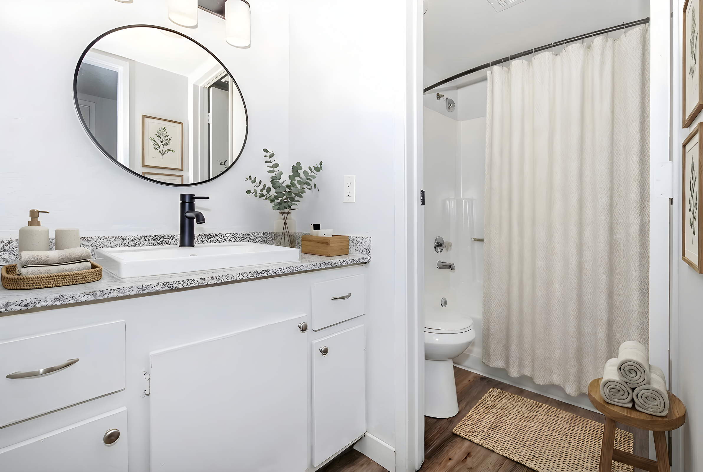 A modern bathroom featuring a large round mirror above a white sink with a dark faucet. The countertop is decorated with plants and soap dispensers. A shower area with a light curtain is visible, along with a toilet and neatly rolled towels on a small shelf. Natural wood flooring adds warmth to the space.