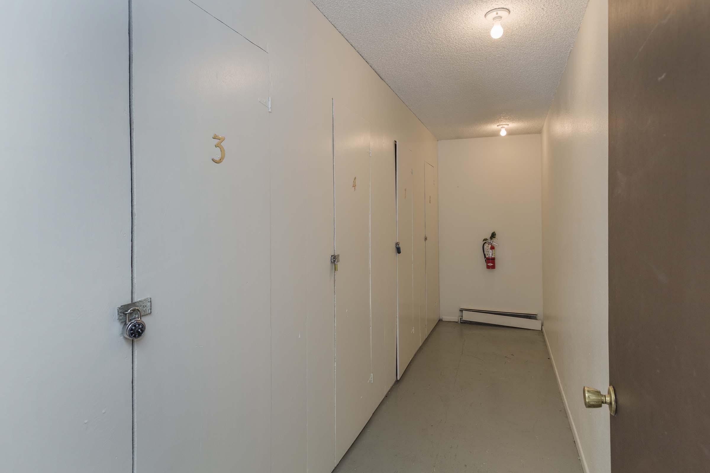Interior hallway of a building, featuring several closed doors numbered 3 and 4. The walls are painted white, and the floor is a light gray. A small fire extinguisher is mounted on the wall. Soft overhead lighting illuminates the space, creating a clean and simple atmosphere.