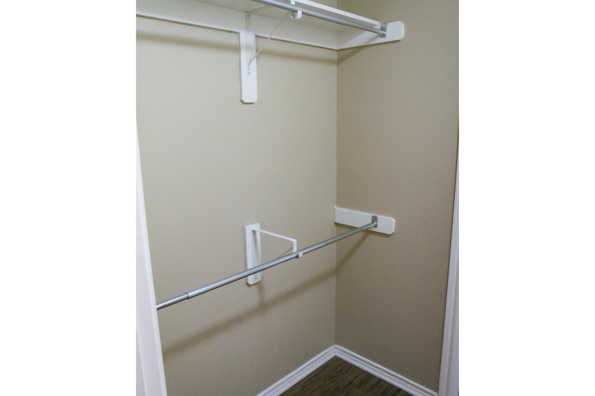 Empty closet with beige walls and a single clothing rod. The floor has a wood-like finish, and there are no items or shelves present, giving it a clean and minimal appearance.