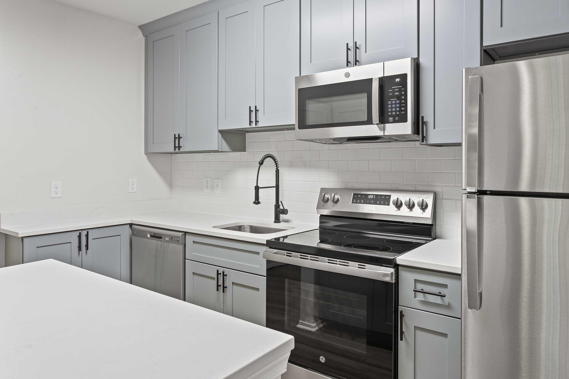 A modern kitchen featuring light blue cabinets, stainless steel appliances, including a microwave and oven, a silver refrigerator, and a white countertop. The design emphasizes a clean, contemporary aesthetic with a minimalist style and a bright atmosphere.