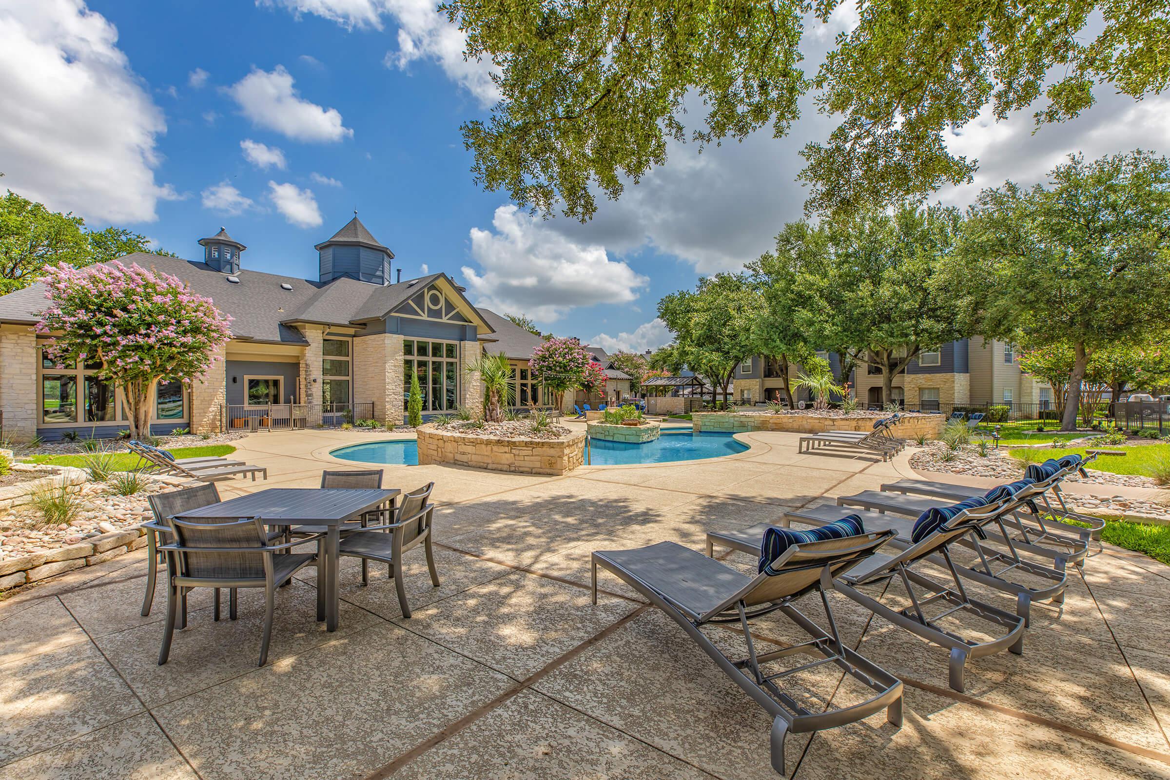 The Falls Round Rock Apartments community pool with a table and chairs