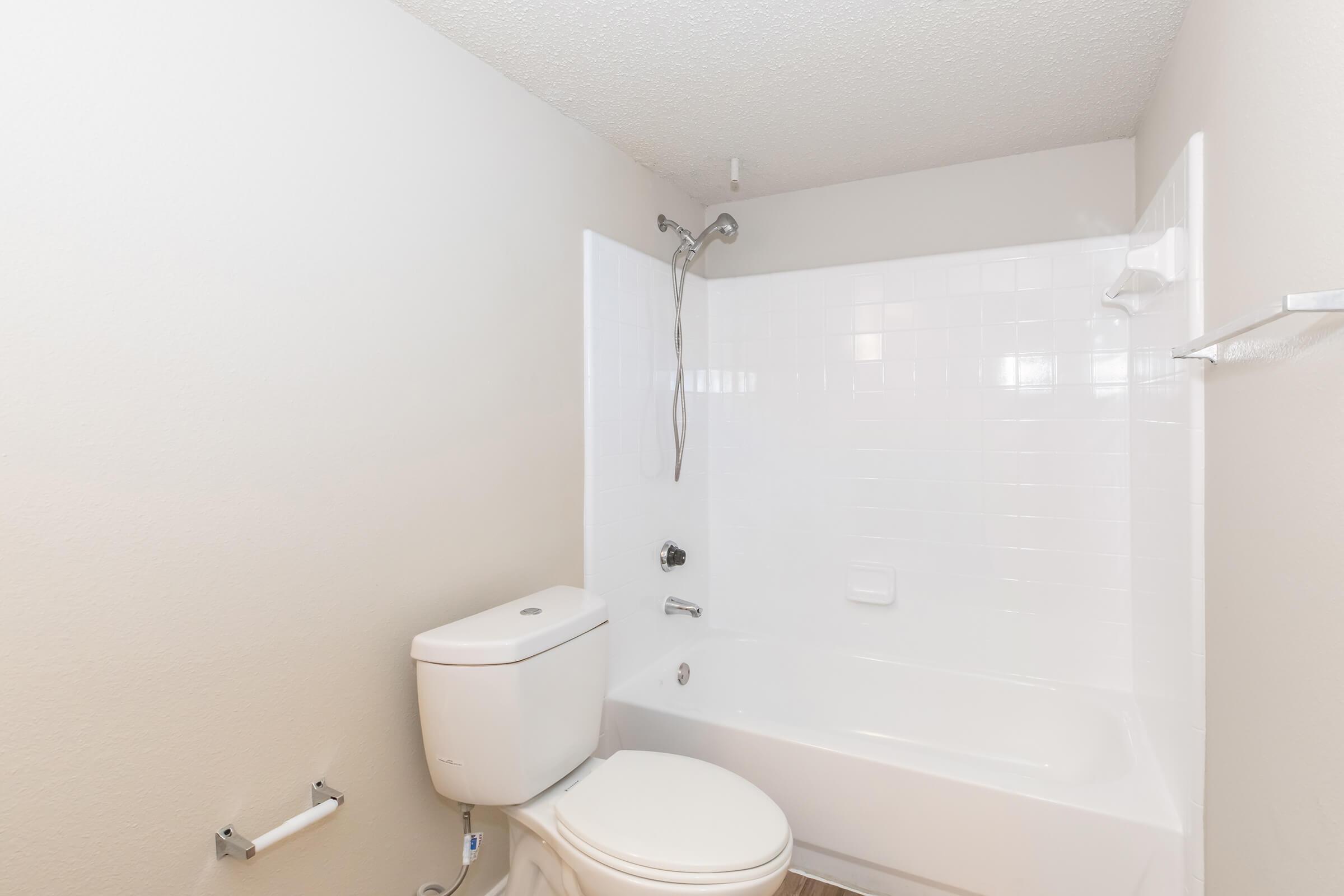 A clean, white bathroom with a bathtub, shower, toilet, and towel rack. The walls are light-colored, and the tile is simple and modern. The space is well-lit and minimalistic, ideal for a fresh and tidy look.