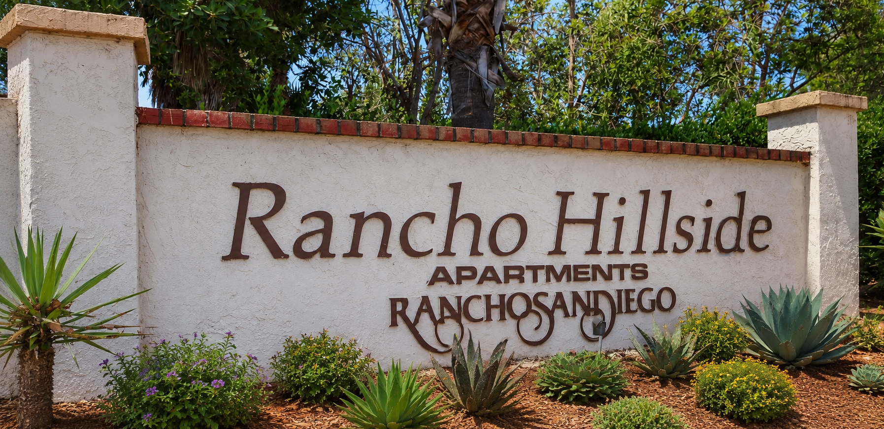 Sign for Rancho Hillside Apartments in Rancho San Diego, featuring decorative plants and landscaping around the entrance.