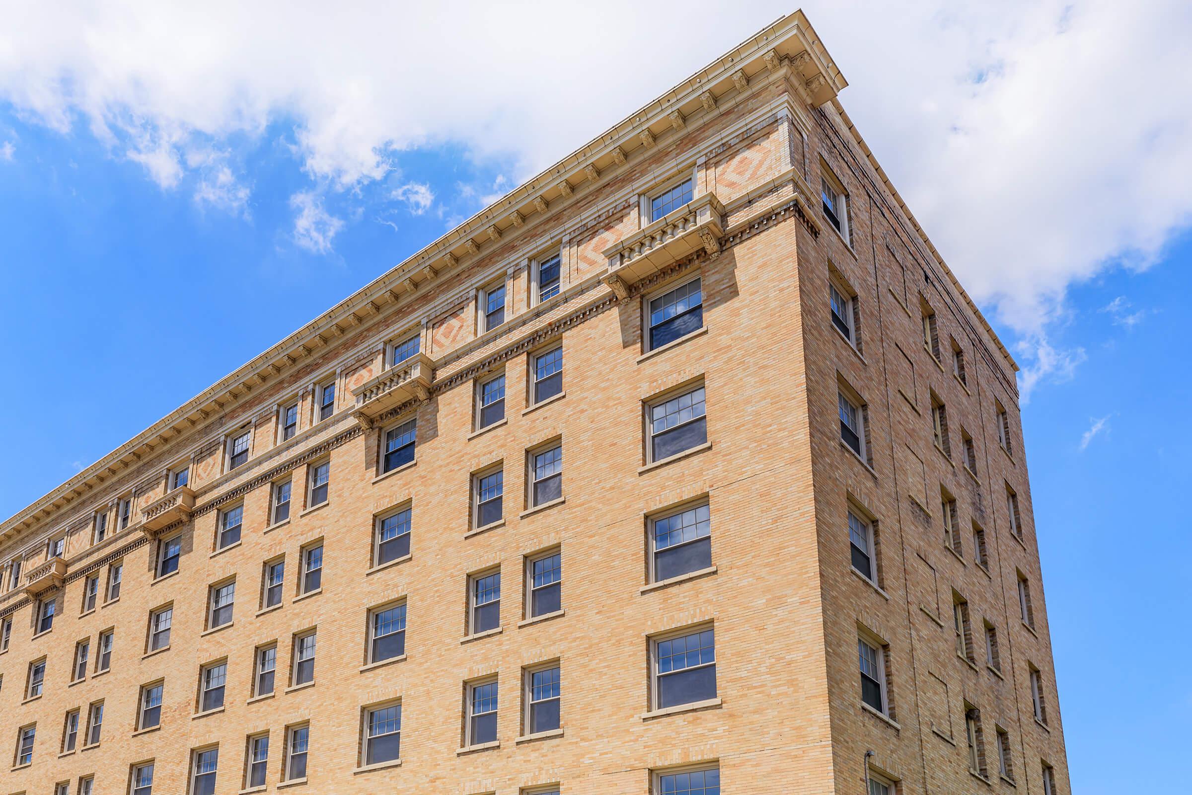 Historic brick building with multiple windows, showcasing architectural details and a blue sky with scattered clouds in the background. The structure has a classic design, emphasizing its height and symmetry.