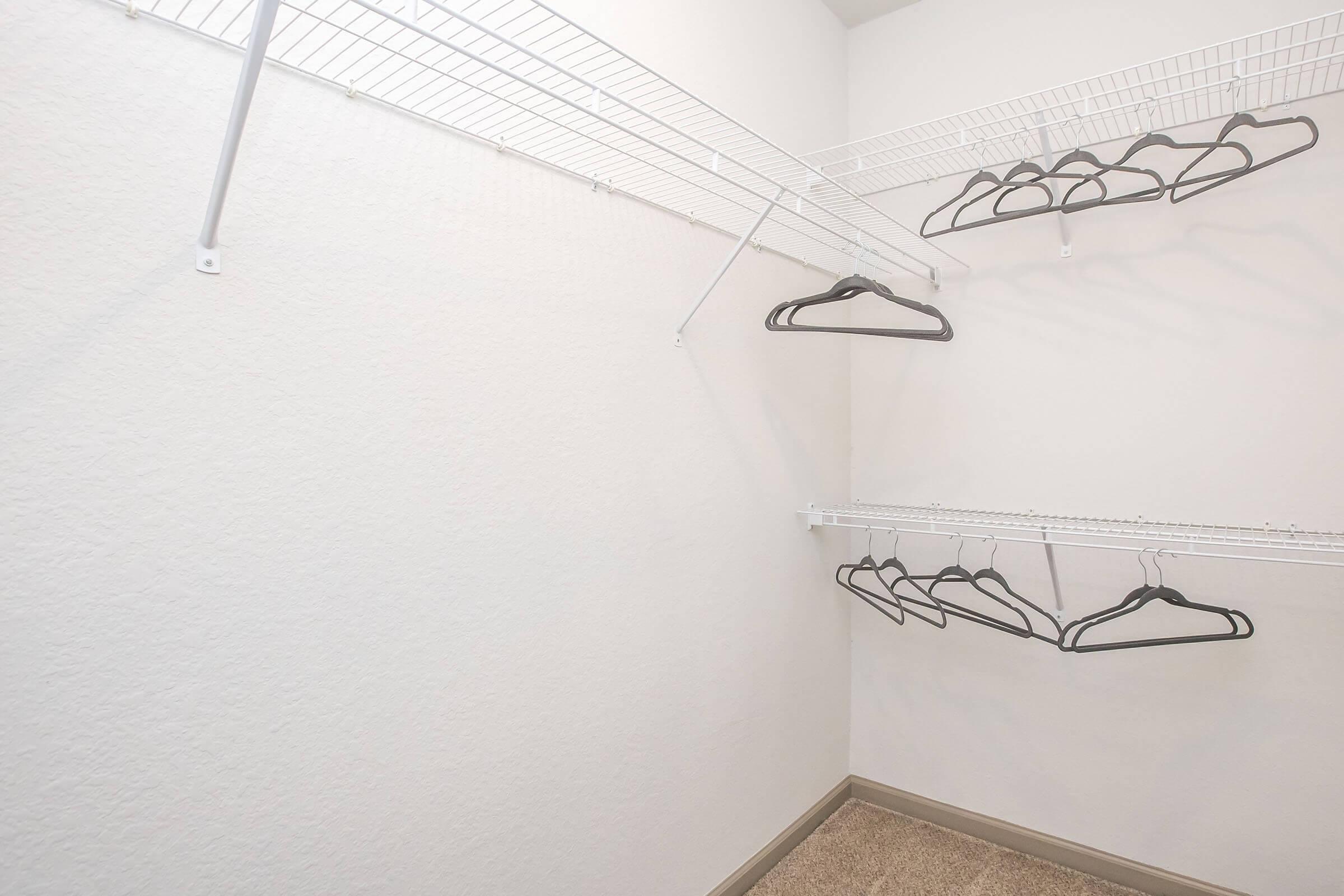 An empty closet with white wire shelving and several empty black hangers. The walls are plain and the floor is carpeted, creating a clean and organized appearance.