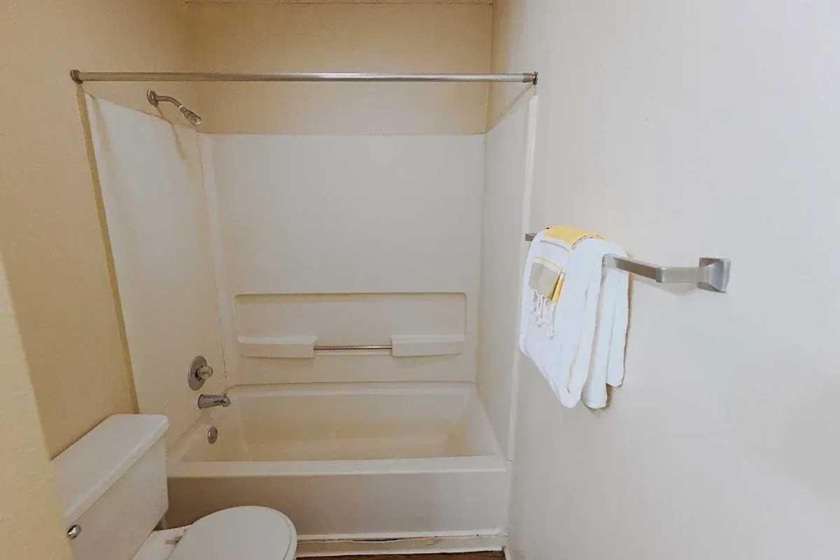 A clean, minimalistic bathroom featuring a shower-tub combo, a toilet, and a towel rack with neatly hung white towels. The walls are painted a light color, enhancing the space's brightness and simplicity.