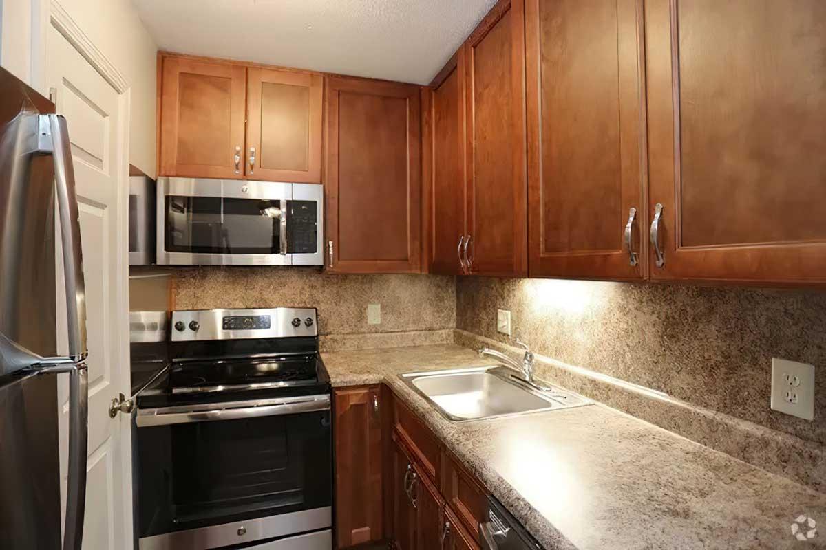 A modern kitchen featuring dark wooden cabinets, stainless steel appliances including a microwave and oven, a double sink, and a countertop with a textured finish. The space is well-lit, highlighting the kitchen's contemporary design and functionality.