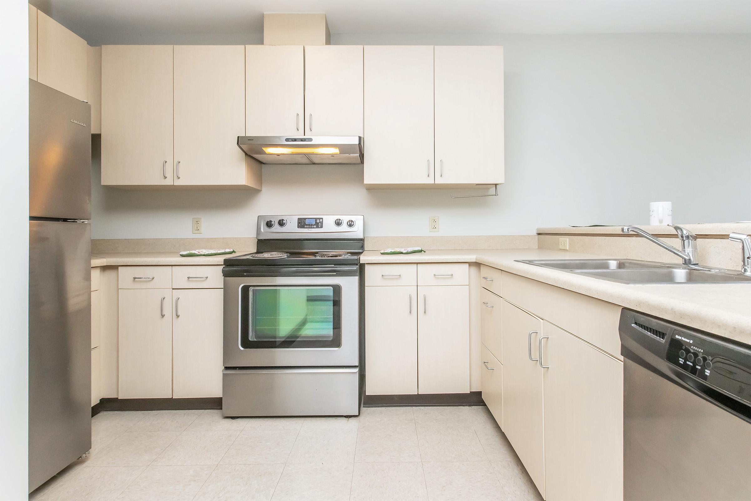 Modern kitchen featuring light-colored cabinets, stainless steel appliances including a refrigerator, oven, and dishwasher, along with a neutral countertop. Adequate countertop space and a simple design create a functional cooking area. Bright lighting enhances the open and airy atmosphere.
