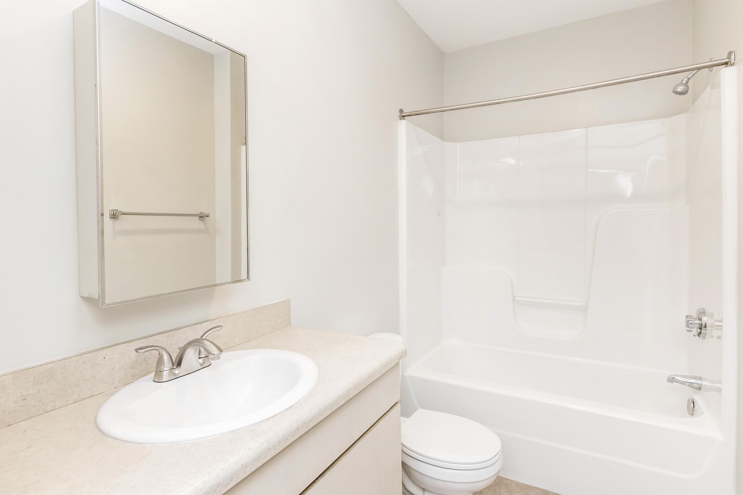 A clean and modern bathroom featuring a bathtub with a shower curtain, a wall-mounted mirror above a sink with a faucet, and a light-colored countertop. The walls are painted in a neutral color, creating a bright and spacious atmosphere.