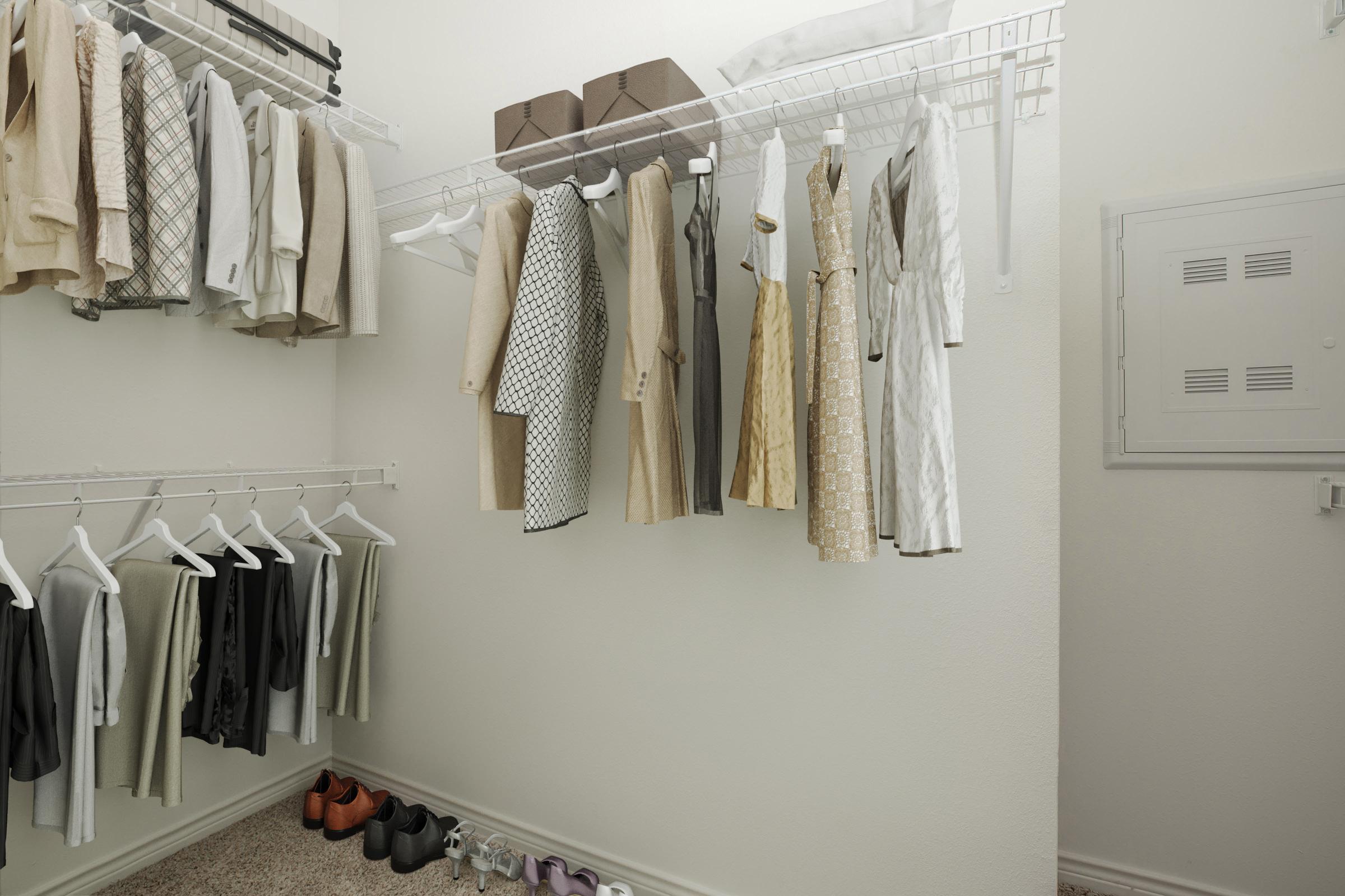 A well-organized walk-in closet featuring various clothing items on hangers, including dresses and suits. The closet is neatly arranged with shoes on the floor and storage boxes on shelves, with light-colored walls and carpeted flooring.