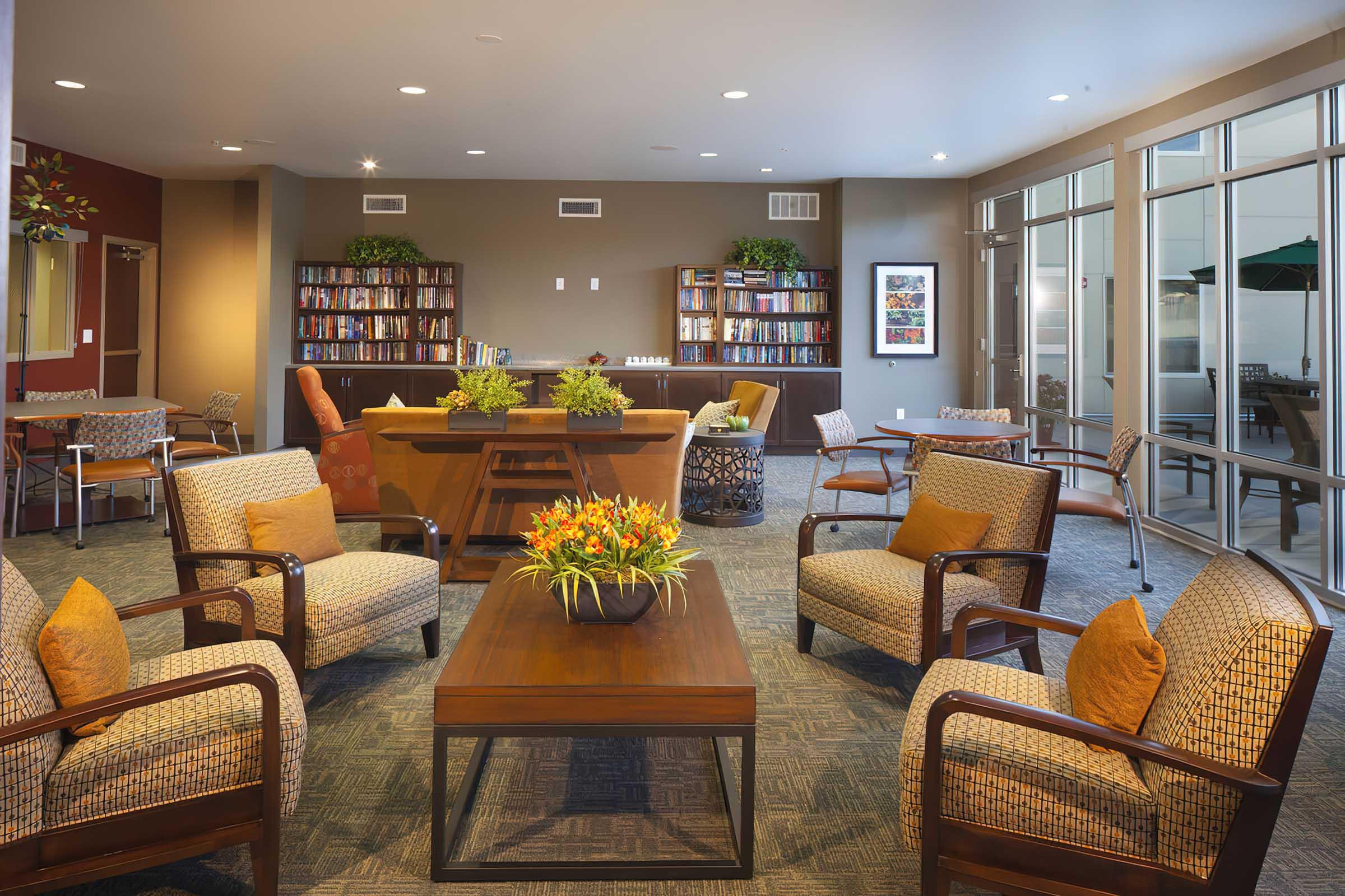 A cozy lounge area featuring comfortable armchairs and a wooden coffee table, surrounded by bookshelves filled with books.