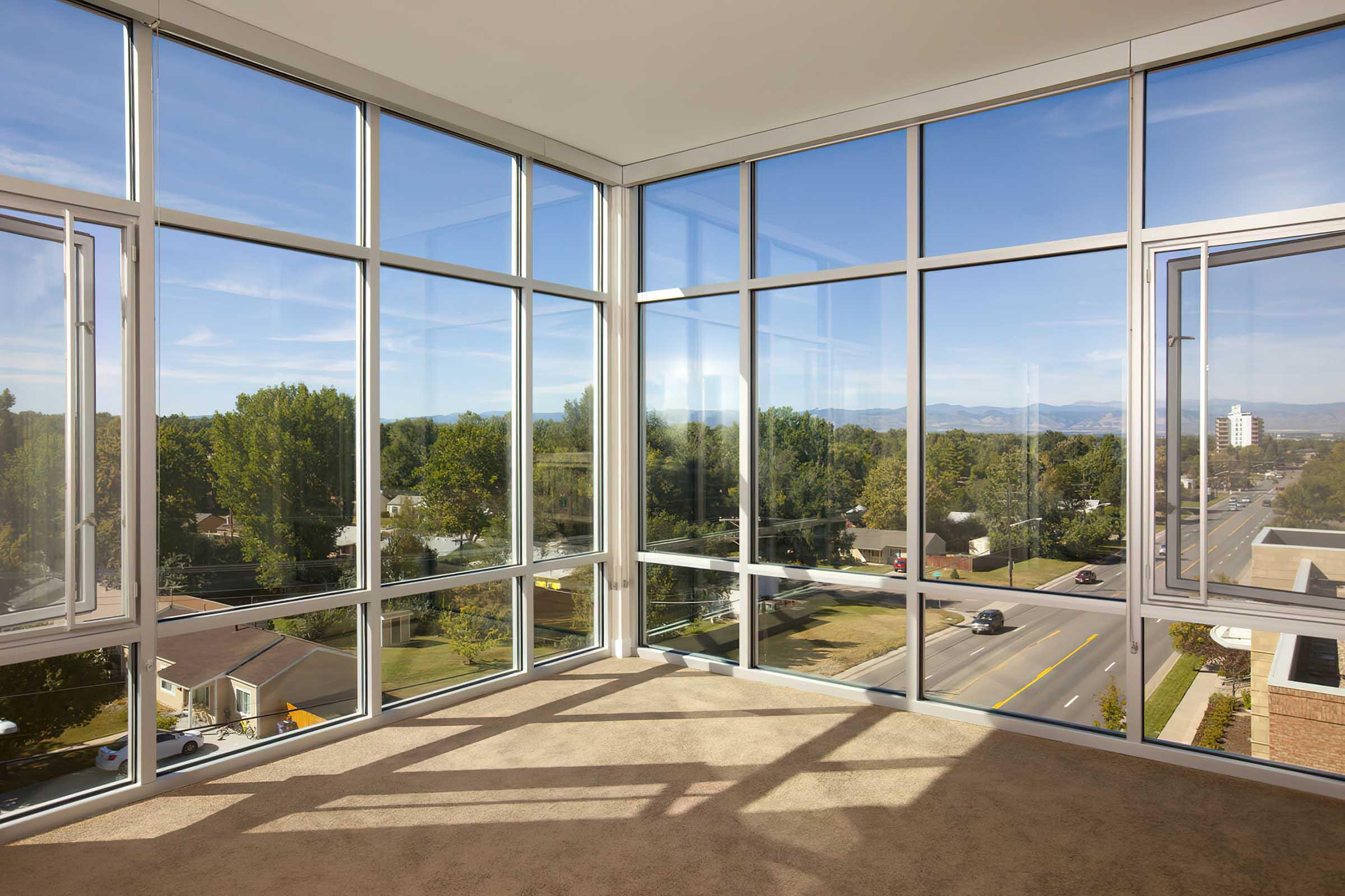 A spacious, modern room with large floor-to-ceiling windows showcasing a clear blue sky and distant mountains.