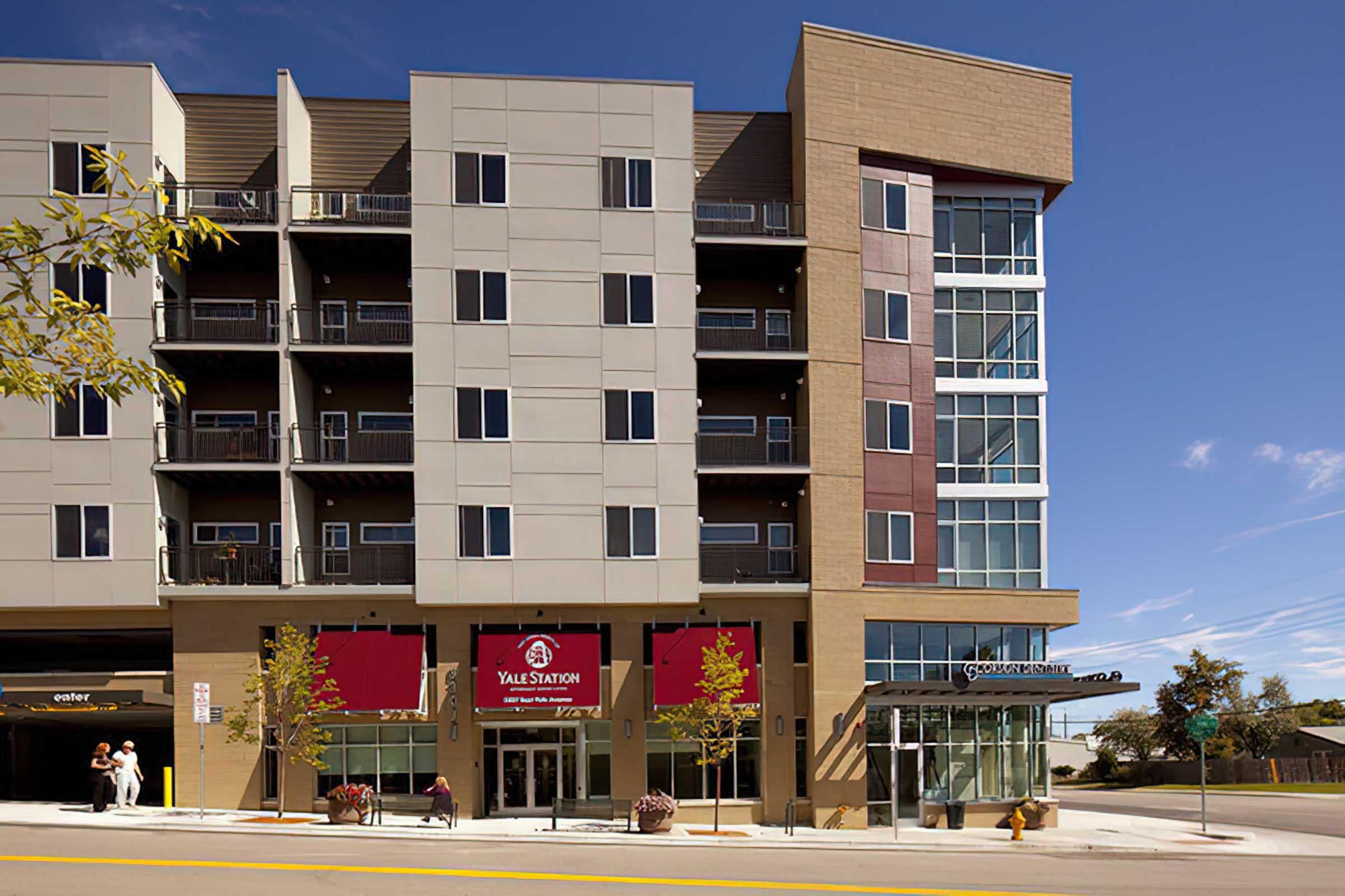 A modern multi-story building with a mix of beige and red panels, featuring large windows and a ground-level entrance marked "Yale Station."
