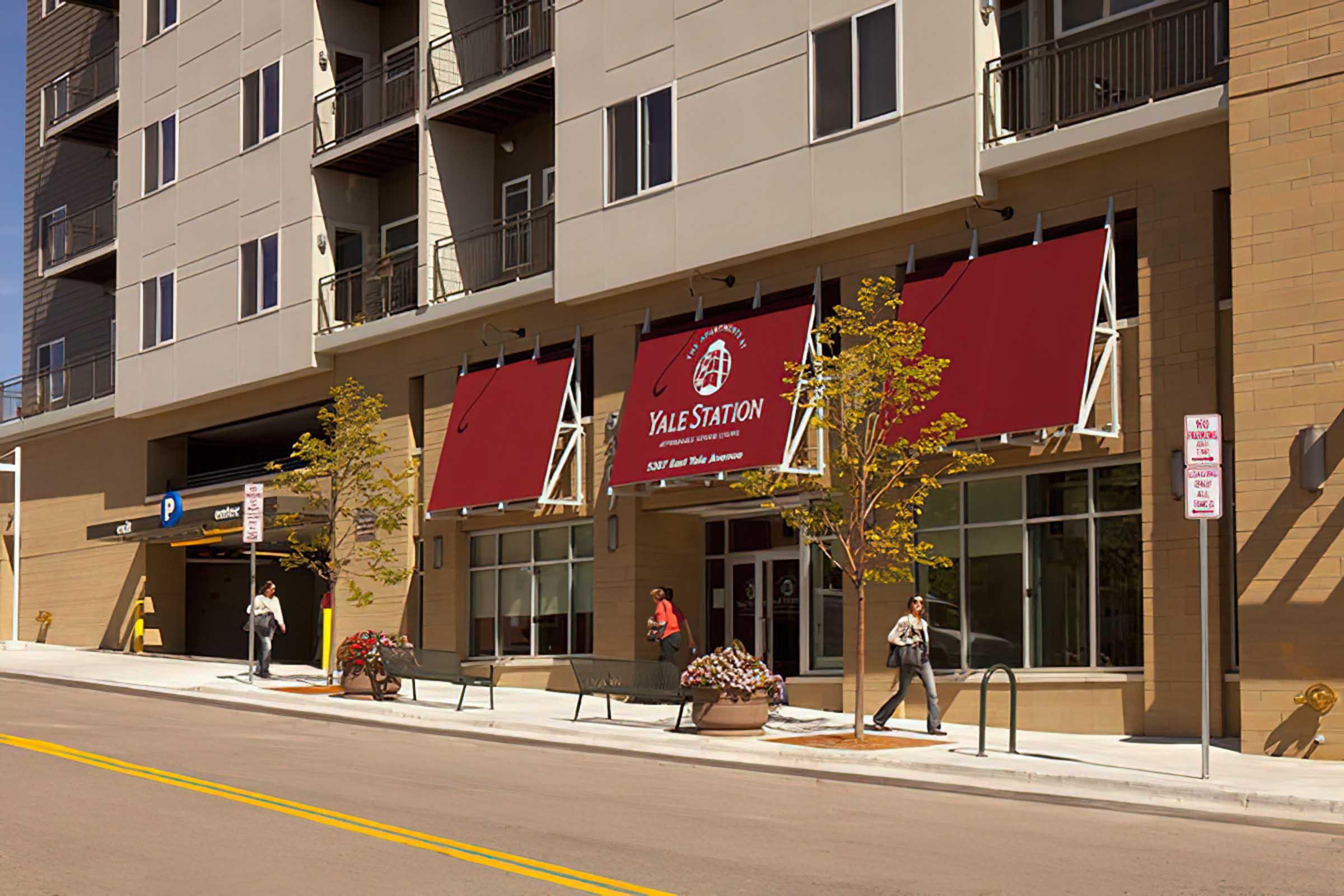 The image shows a modern building exterior with large windows and red awnings displaying "YALE STATION."