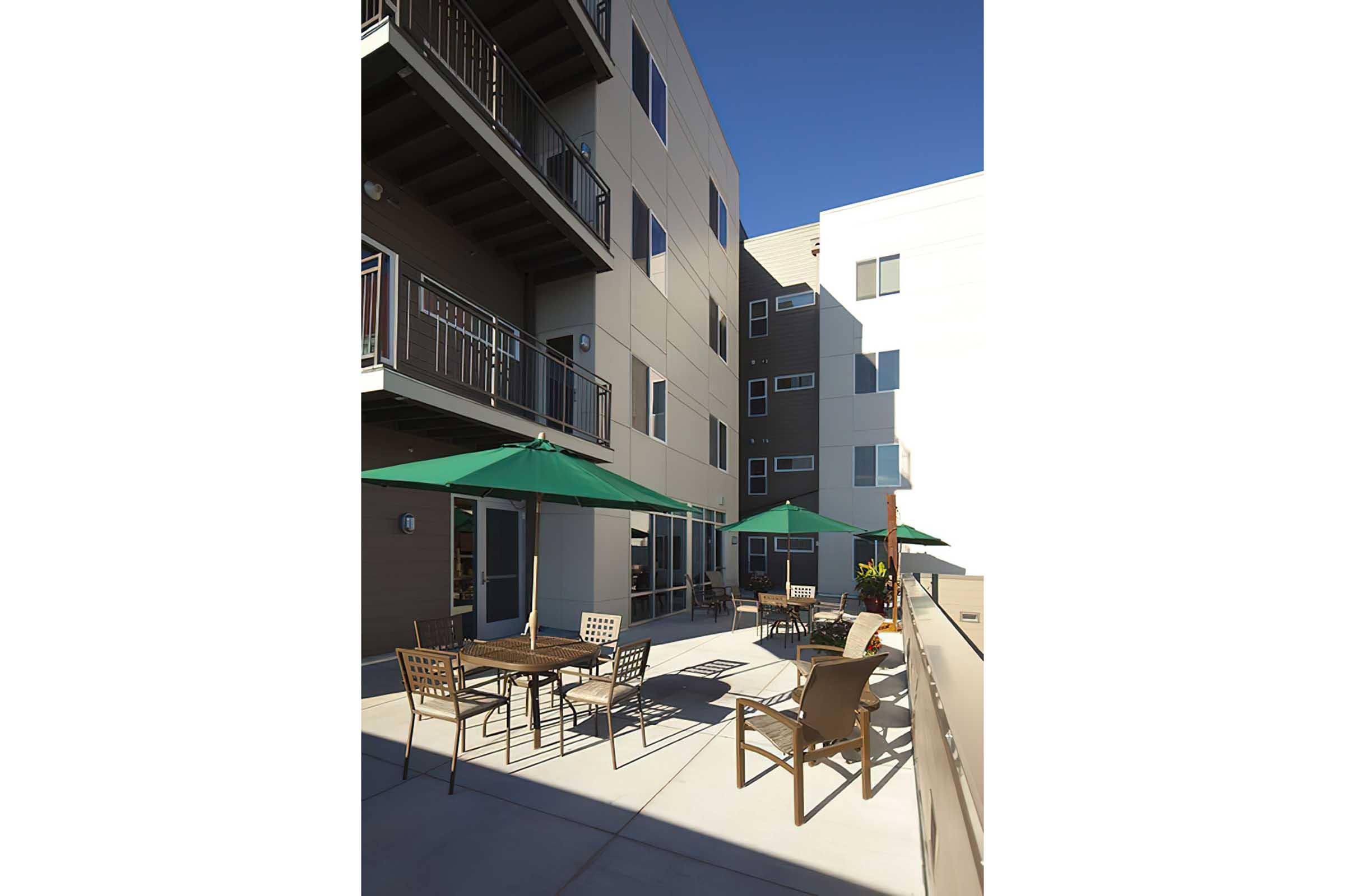 A modern outdoor area with tables and chairs under green umbrellas.