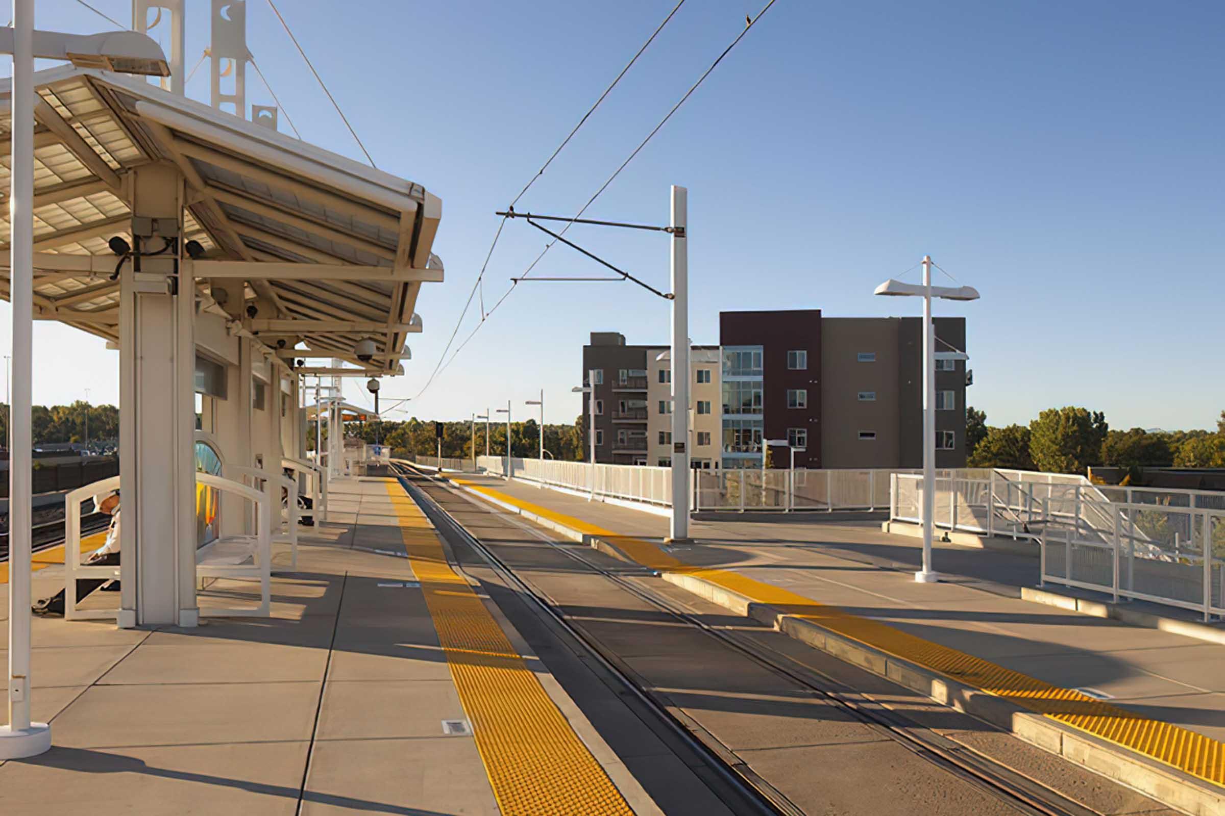 An empty light rail station platform with rail tracks, yellow safety strips, and modern seating.