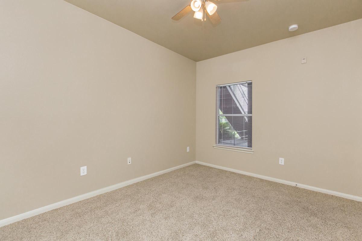 Bedroom with tan carpet, ceiling fan, and window with blinds