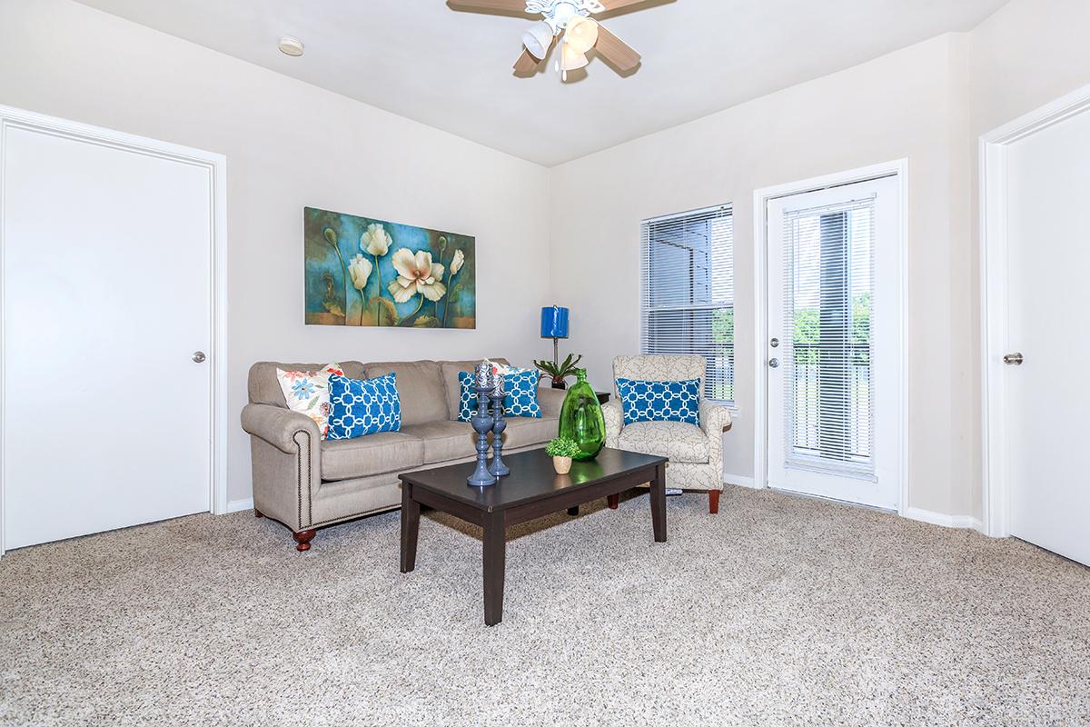 Sofa, armchair and coffee table in carpeted living room with door to private balcony