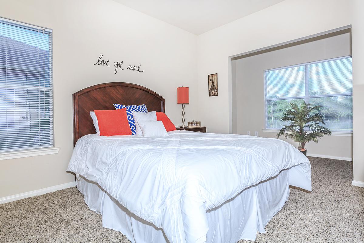 Carpeted bedroom with double bed and three large windows with blinds