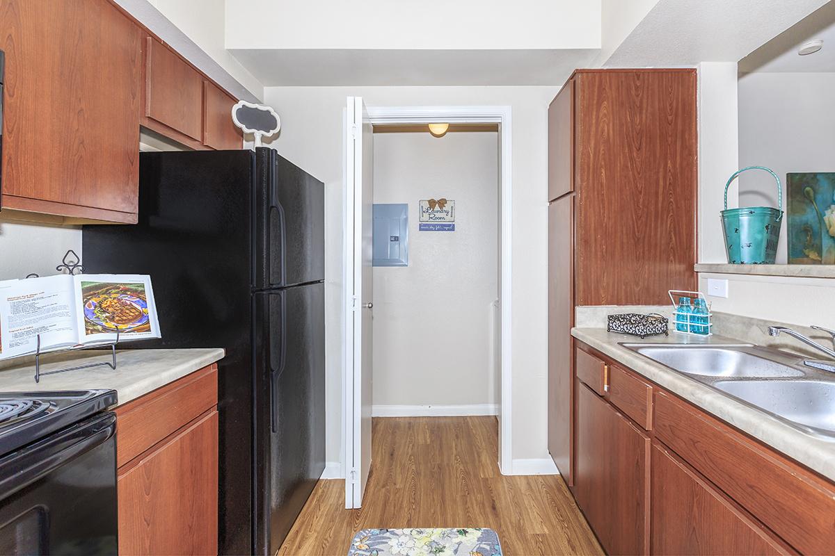Galley-style kitchen with brown cabinetry, black appliances, and access to full-size washer/dryer