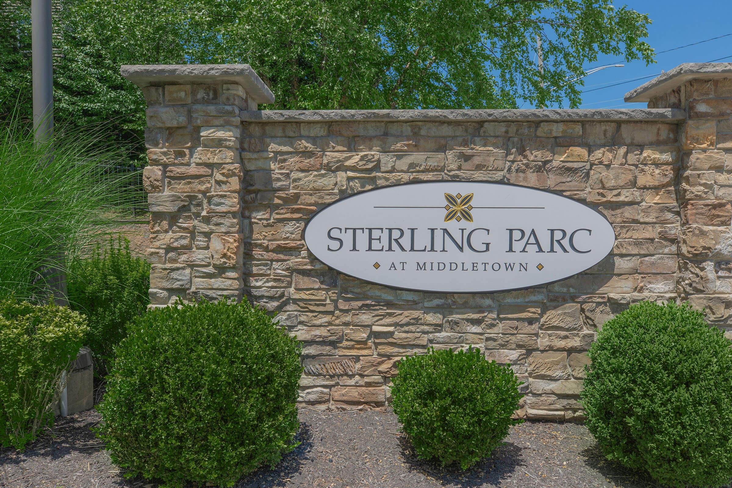 Sign for "Sterling Parc at Middletown" set on a stone wall, surrounded by neatly trimmed greenery. The entrance is inviting, with natural elements providing a welcoming atmosphere.