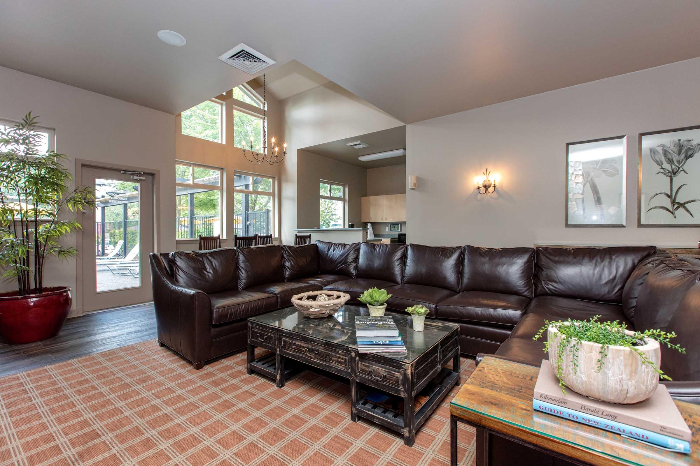 A cozy living room featuring a large brown sectional sofa, a wooden coffee table with decorative items, indoor plants, and a warm color palette. Large windows provide natural light, illuminating the modern decor and inviting atmosphere.