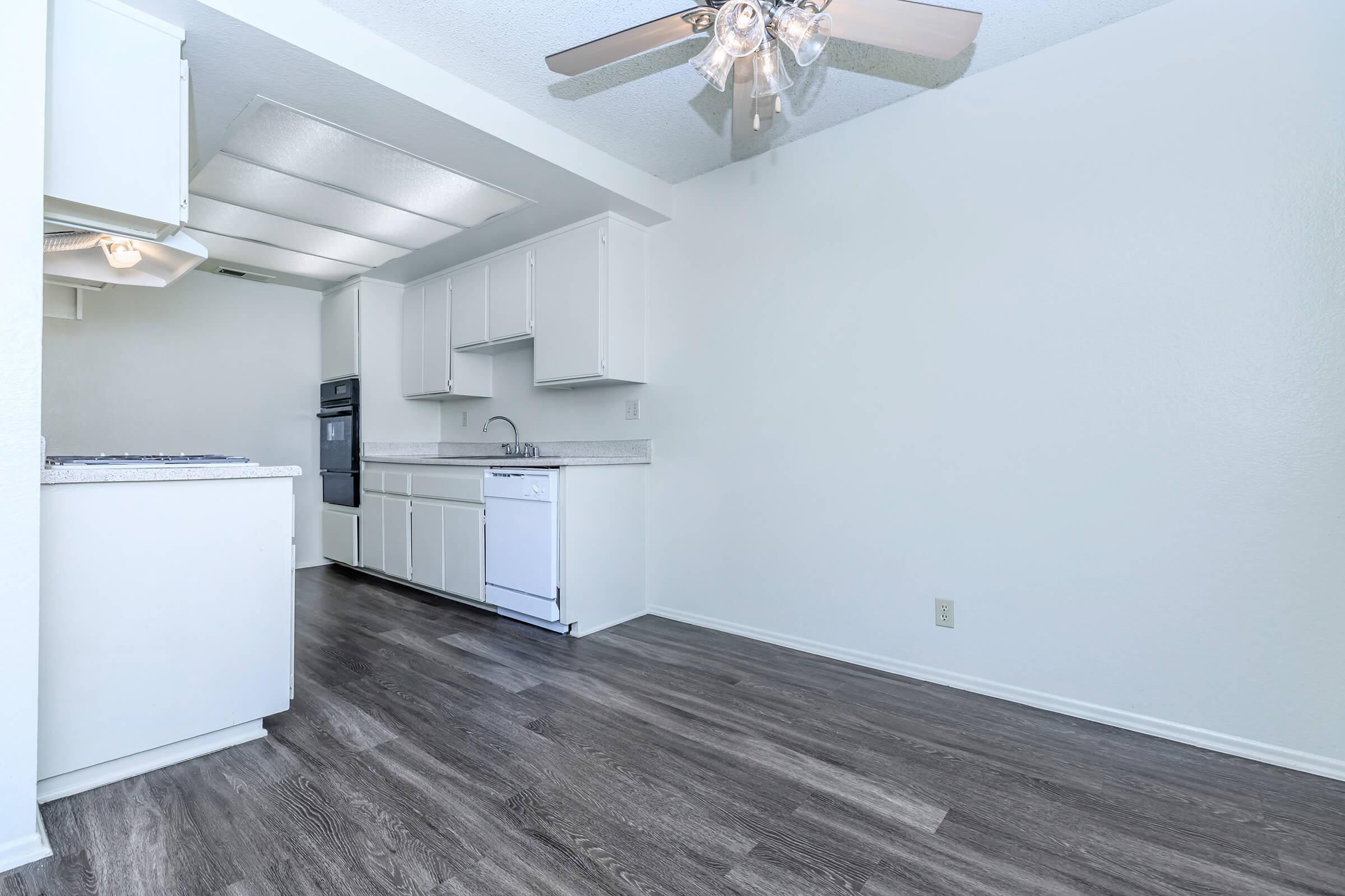 A clean and modern kitchen featuring white cabinets, a black refrigerator, and a countertop. The space includes a ceiling fan, attractive laminate flooring, and recessed lighting. The walls are painted light colors, providing a bright and airy atmosphere.