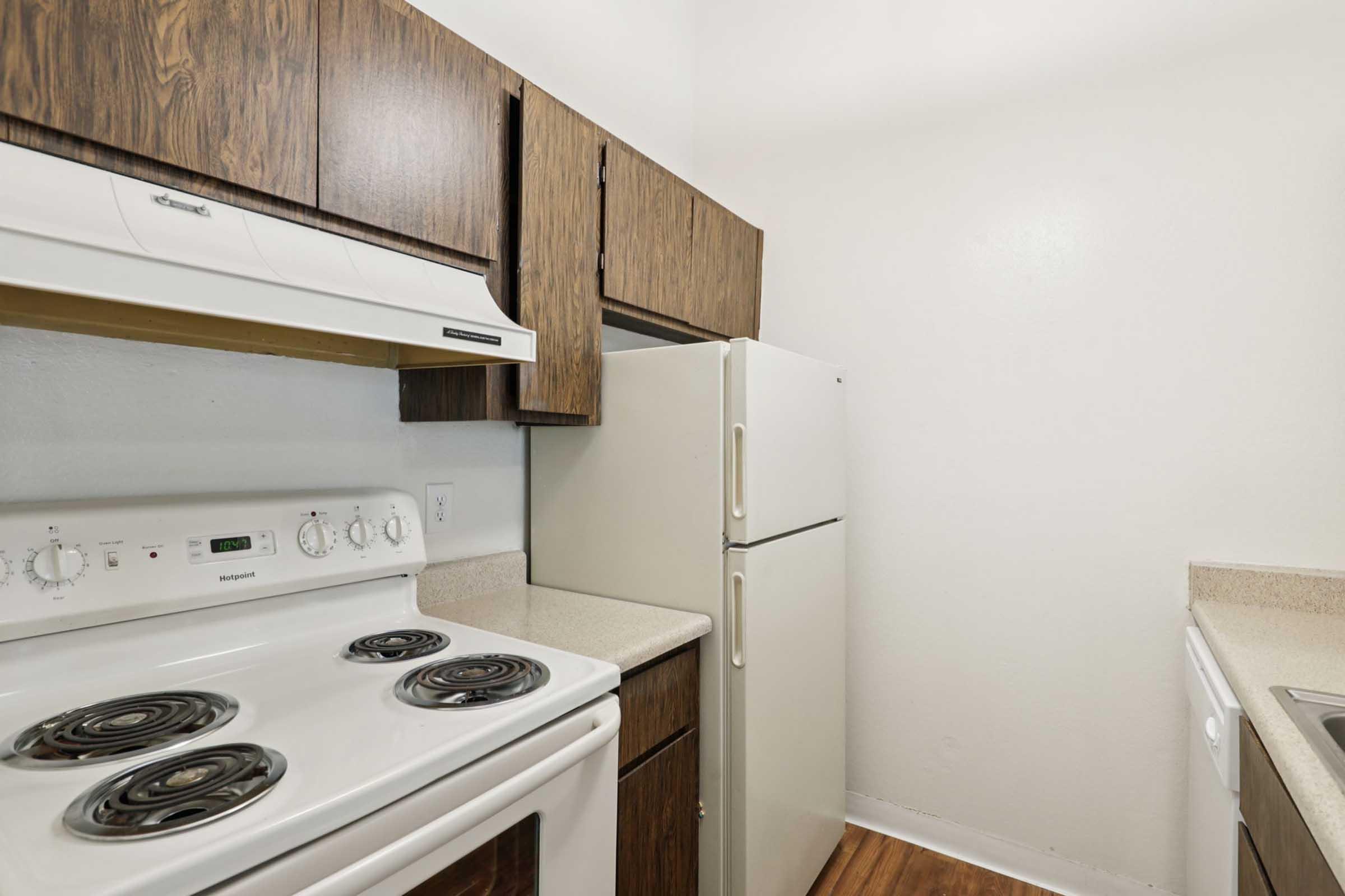 A small kitchen featuring dark wood cabinetry, a white electric stove with four burners, a white refrigerator, and a countertop. The walls are painted light colors, creating a bright and functional space. The floor appears to be wood laminate.