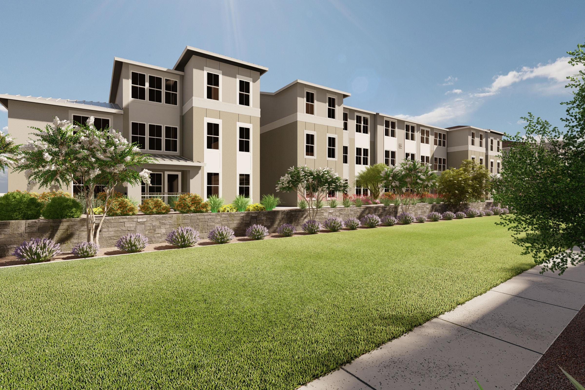 A modern multi-story residential building set against a clear blue sky, surrounded by well-maintained landscaping. The foreground features a lush green lawn and a pathway, while plants and shrubs line the property, enhancing the inviting atmosphere of the community.