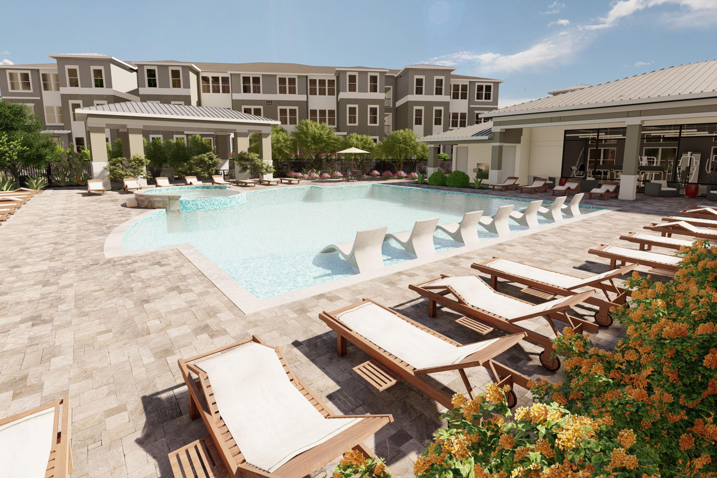 A spacious pool area featuring a clear blue swimming pool surrounded by lounge chairs on a tiled patio. Lush greenery and colorful flowers are visible along the edges. In the background, there are modern apartment buildings, and the sky is bright with a few clouds. Ideal for relaxation and leisure.