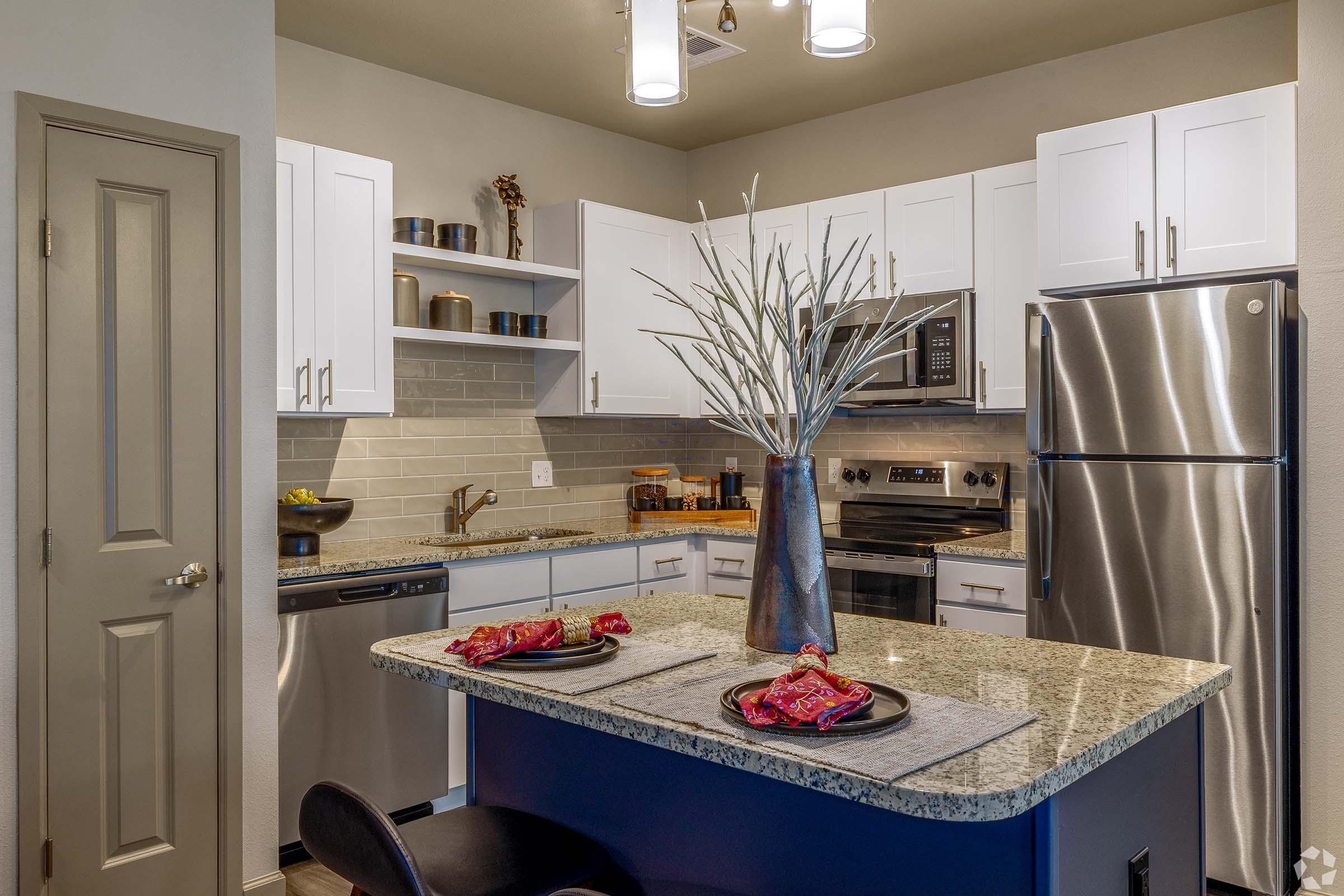 Modern kitchen featuring white cabinets, stainless steel appliances, and granite countertops. A centerpiece with decorative branches sits on a kitchen island. Table settings with colorful napkins are placed on the counter, creating a stylish and functional space.