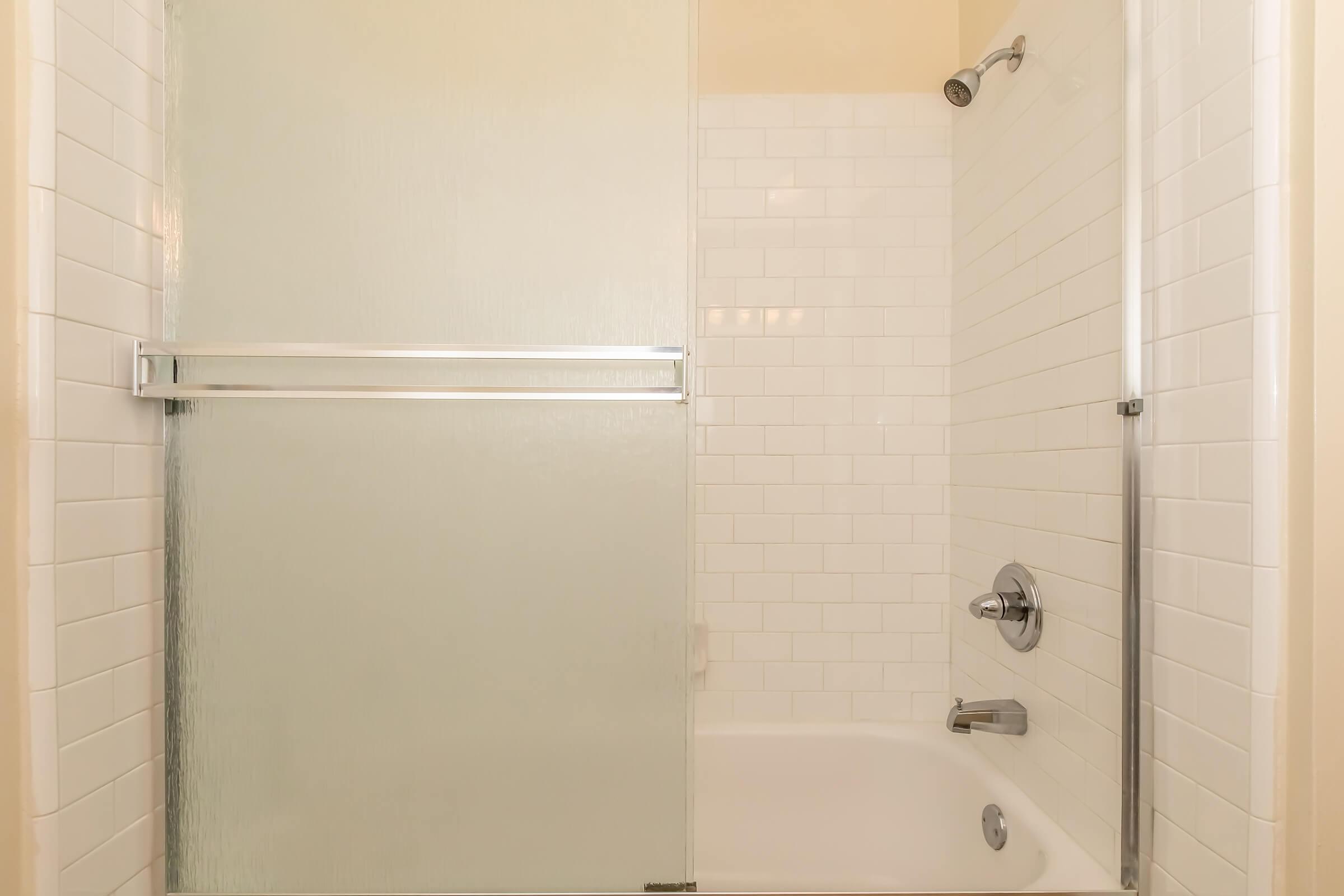 Bathroom featuring a clean, modern shower area with a glass sliding door. The walls are tiled with white subway tiles, and there is a bathtub visible beneath the shower. The fixtures are sleek and contemporary, creating a bright and airy atmosphere.