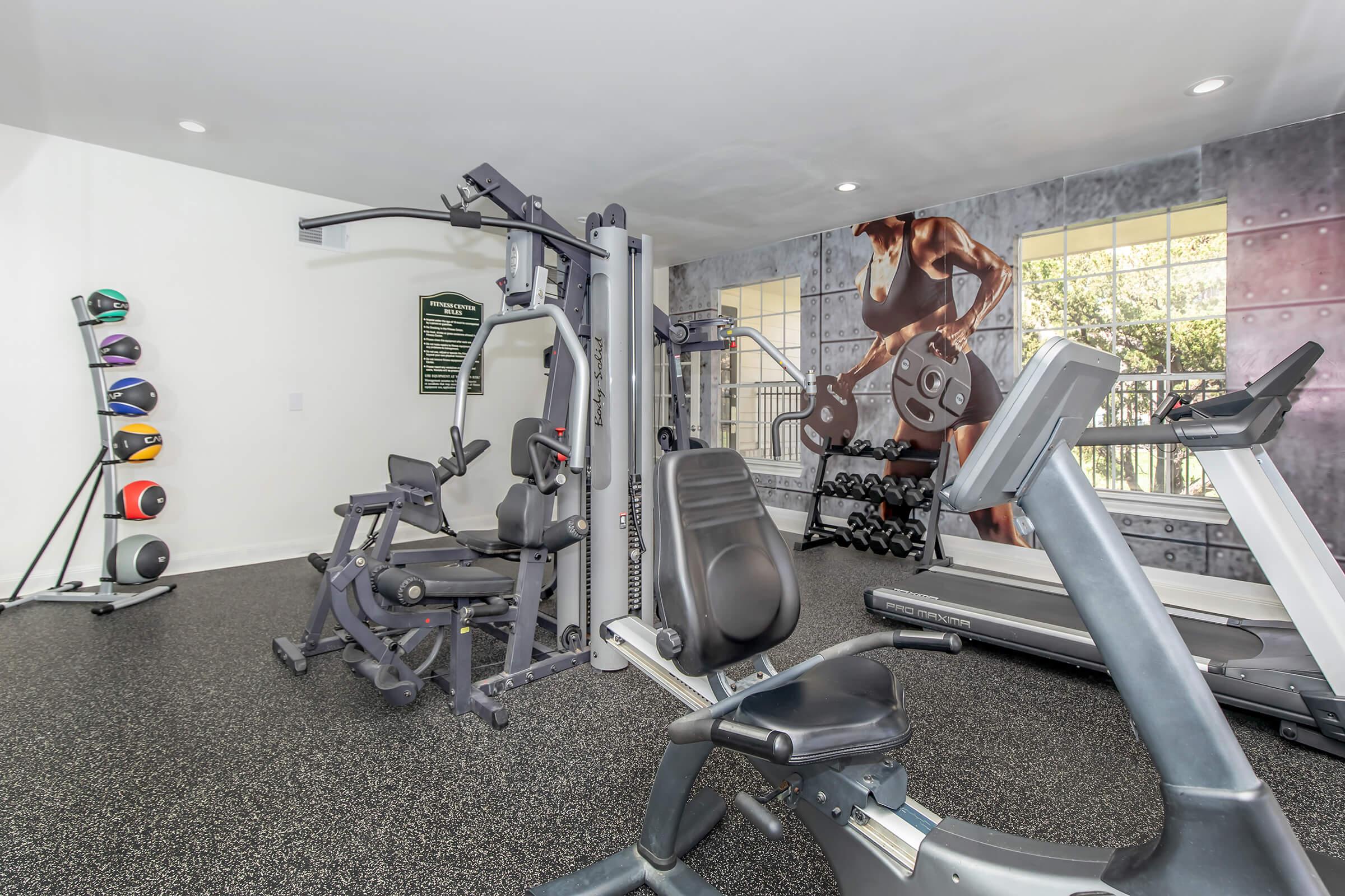 A modern gym interior featuring various workout equipment, including a multi-station machine, a treadmill, and free weights. The walls are decorated with motivational imagery and exercise-related details, creating an inviting atmosphere for fitness enthusiasts.
