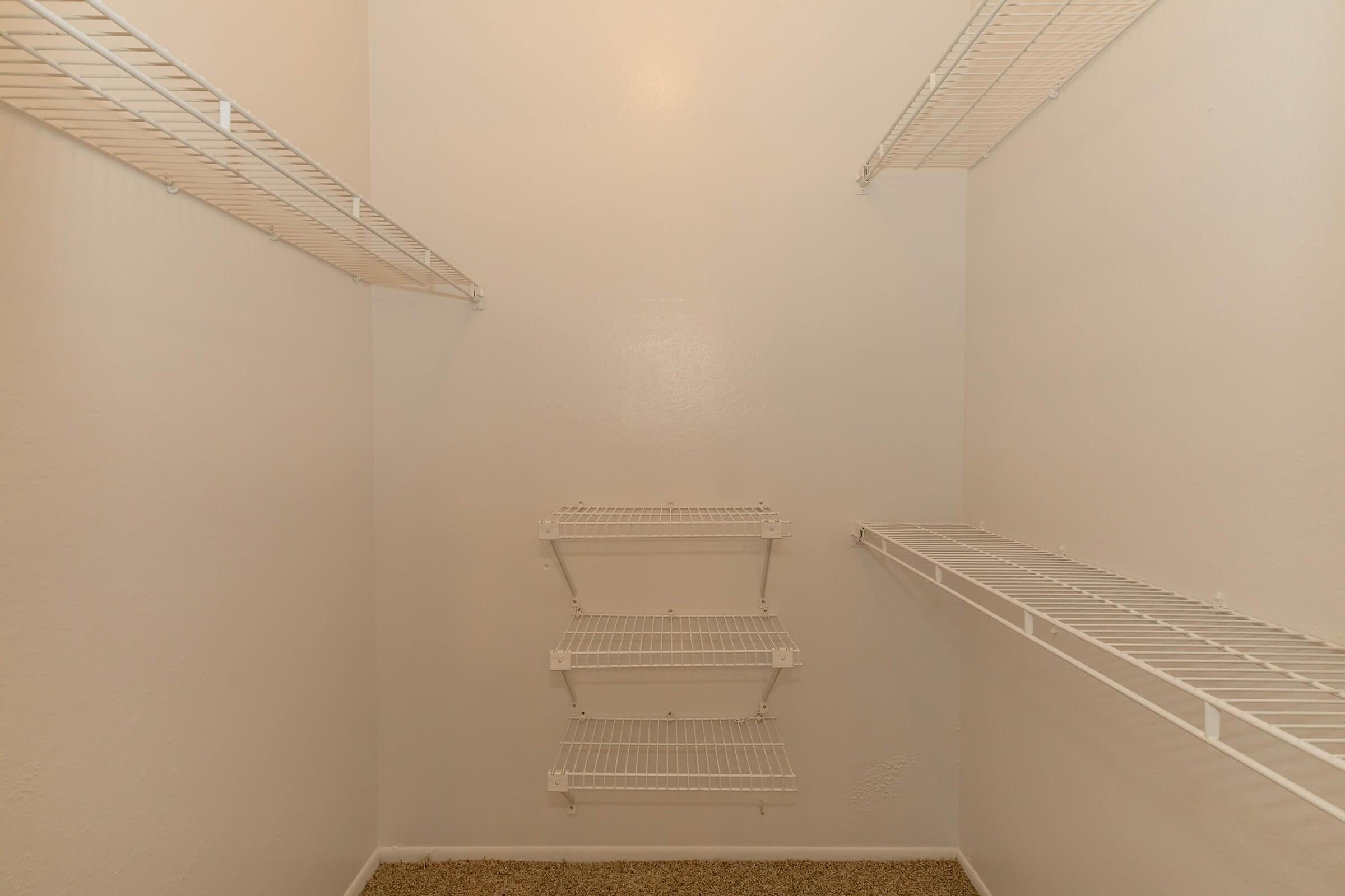 Empty closet with white walls and several wire shelves mounted on the sides. The floor is covered with beige carpeting.