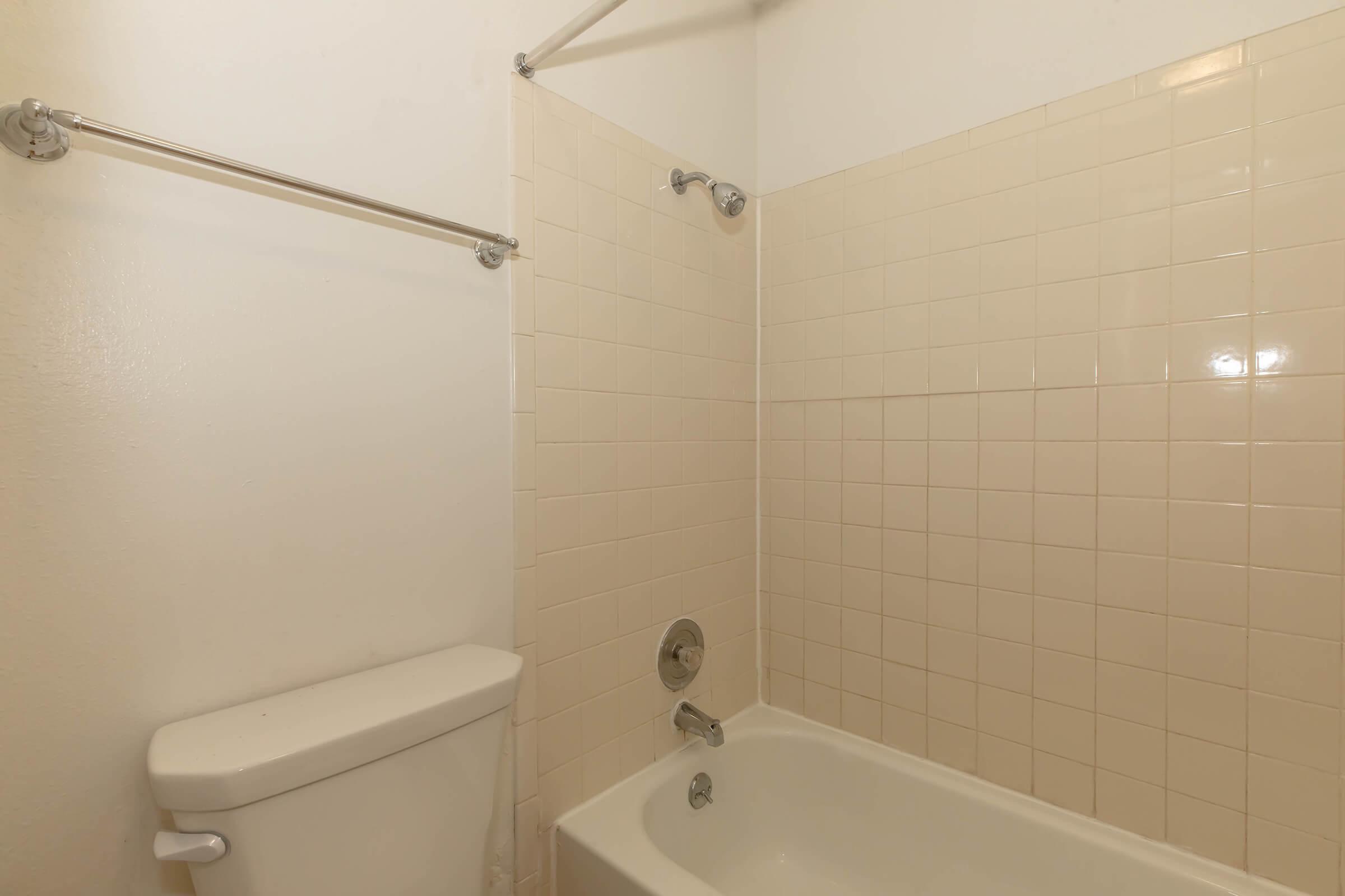 A clean bathroom with a bathtub, shower fixtures, and white tiled walls. There is a toilet next to the bathtub, and the space has a simple design with neutral colors.