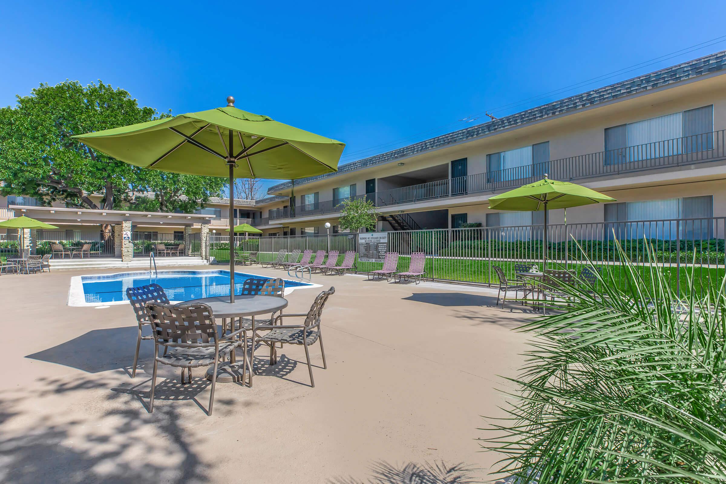 Kimberly Arms Apartment Homes community pool with tables and green umbrellas