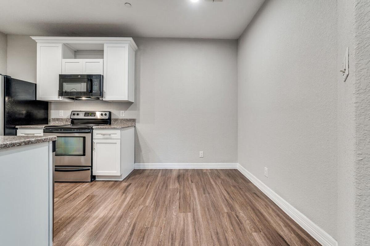 Modern kitchen featuring stainless steel appliances, including a stove, microwave, and refrigerator. White cabinets and granite countertops provide a clean, bright look. The floor is made of wood-like laminate, giving a warm feel. The walls are painted in a light gray, adding to the contemporary ambiance of the space.