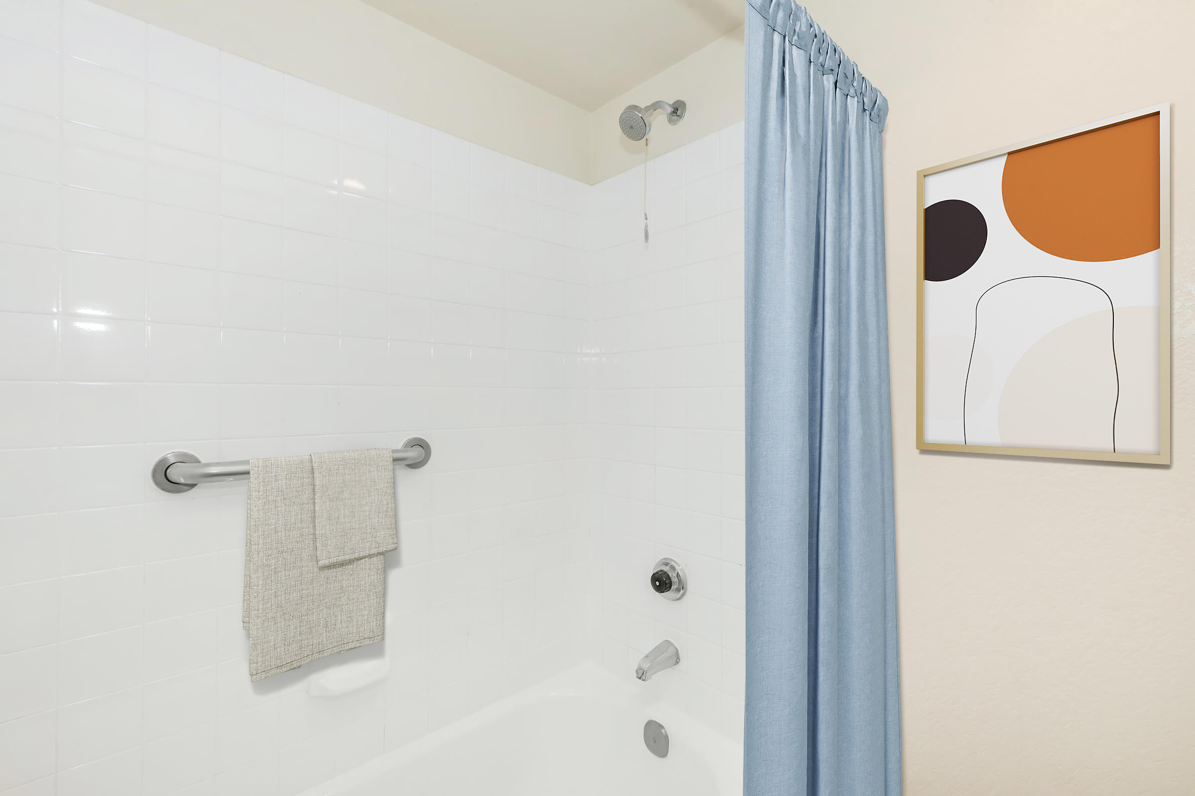 A clean, modern bathroom featuring a bathtub with a shower curtain in light blue. There’s a towel hanging on a silver bar and an abstract art piece framed on the wall, displaying earthy tones of orange, beige, and white. The tiles have a glossy finish, adding brightness to the space.